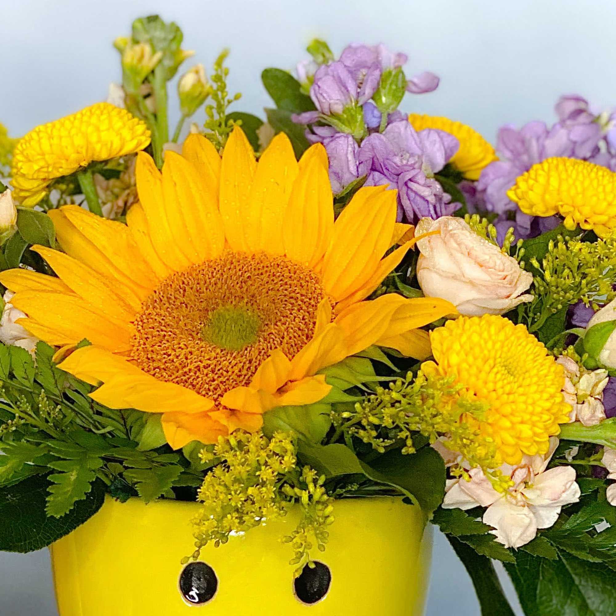 Yellow sunflower bouquet with purple and white flowers in a yellow container