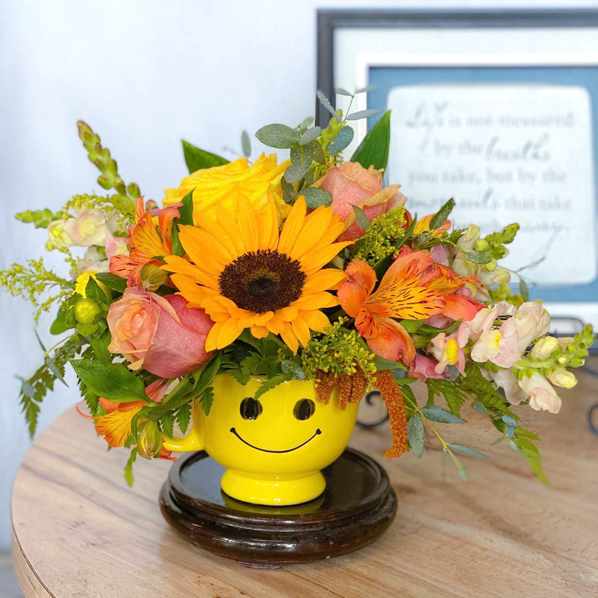 Sunflower and rose arrangement in a yellow smiley-face mug