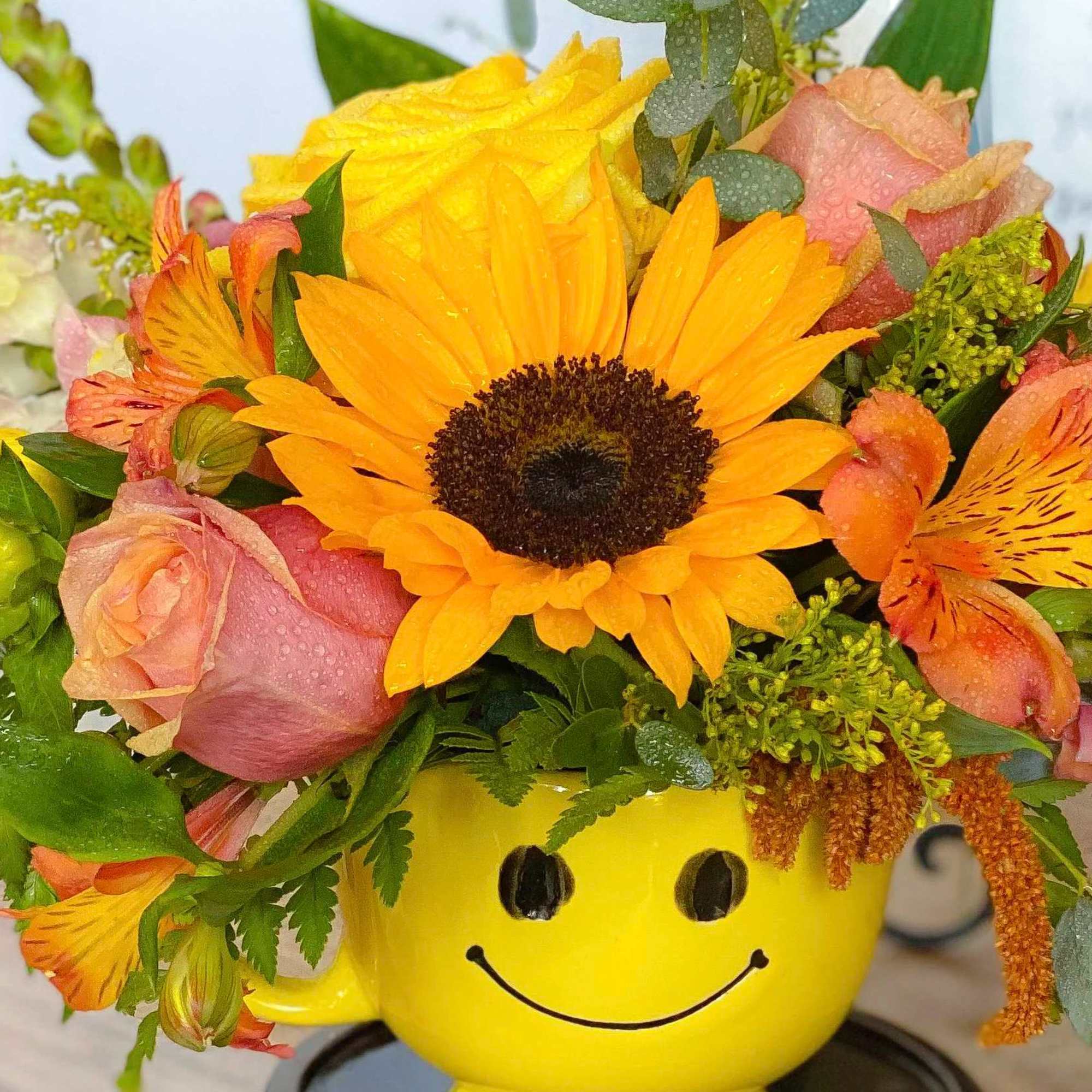 Bouquet of sunflowers and pink roses in a yellow smiley-face mug