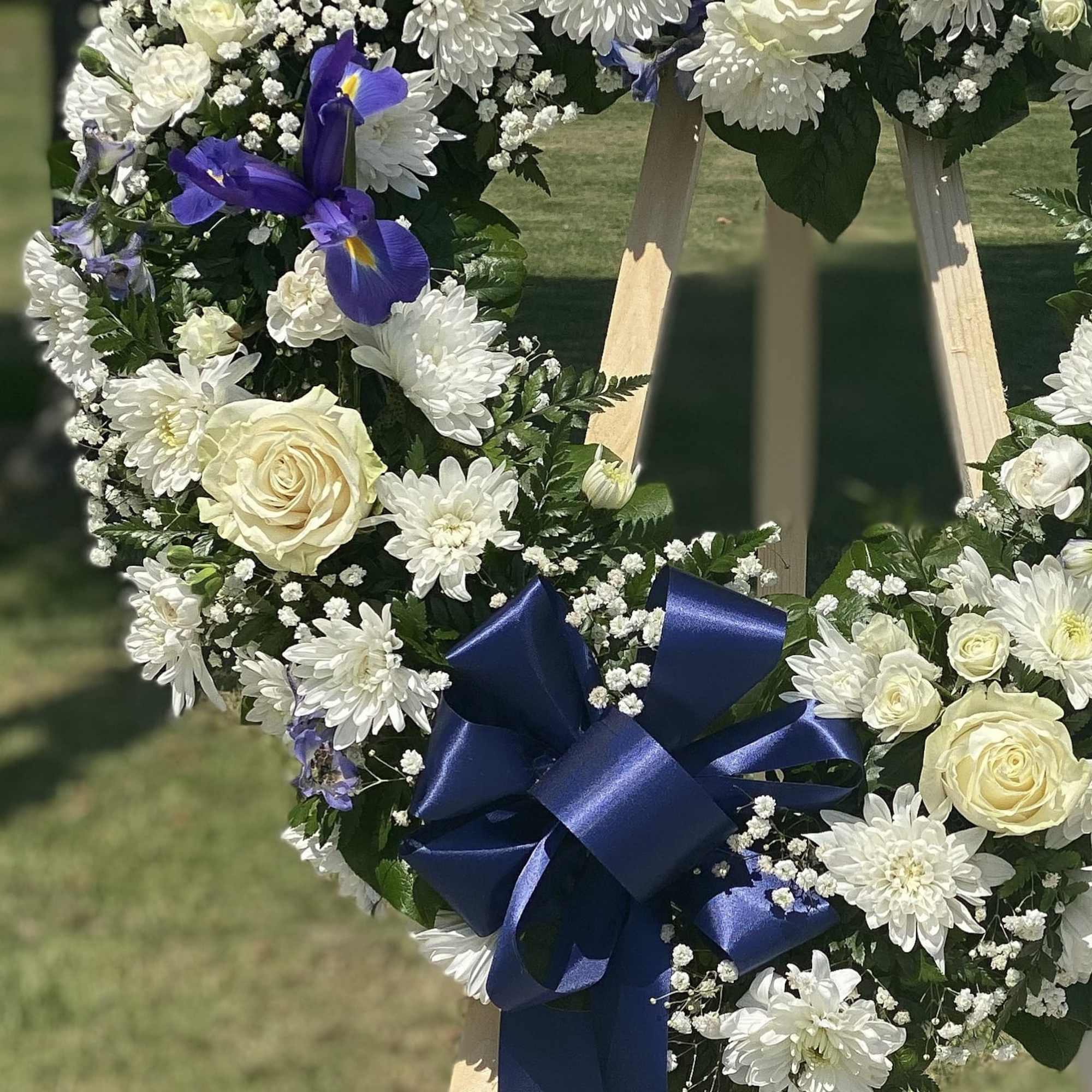 Floral wreath with white flowers, cream roses, purple irises, and a blue ribbon
