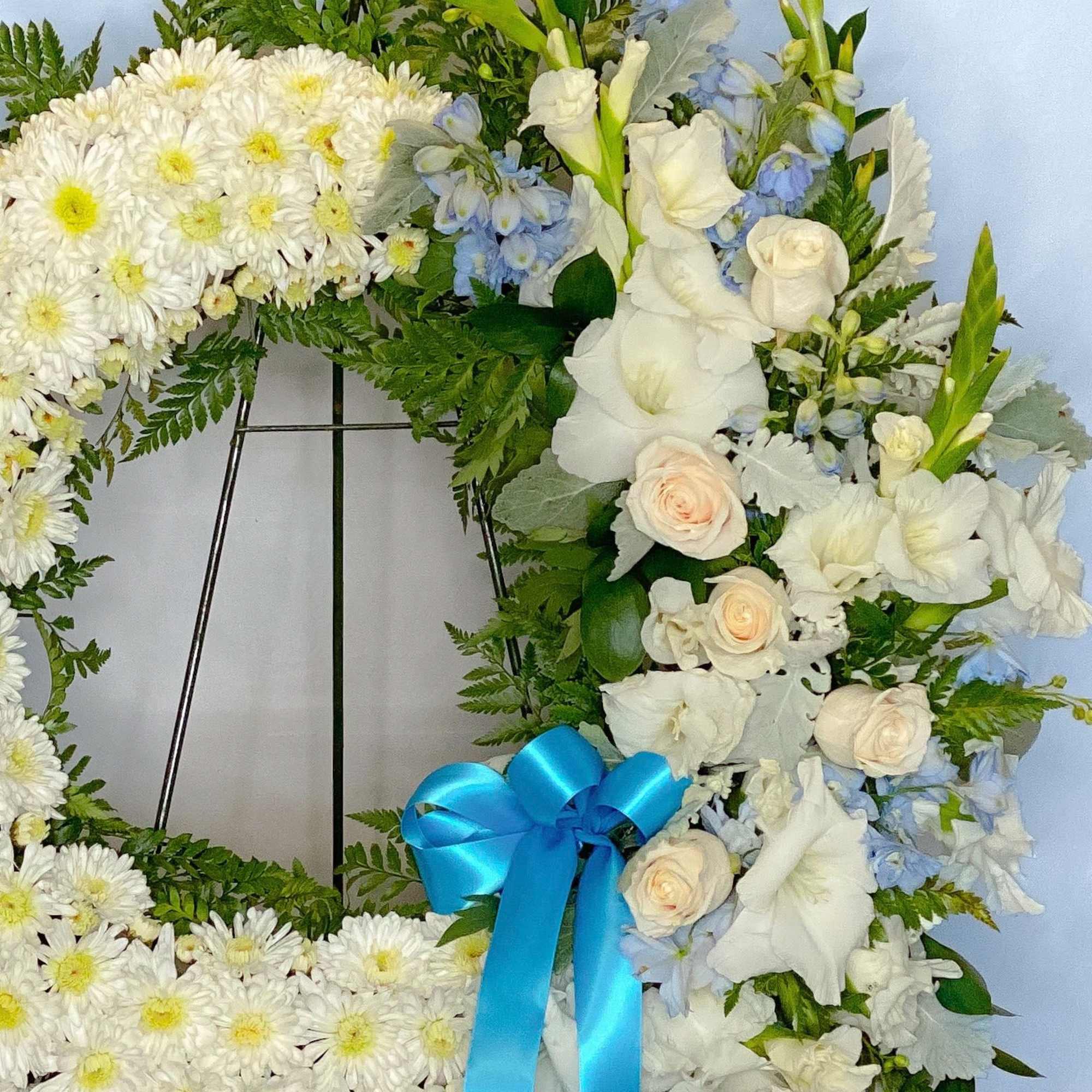 White floral wreath with a blue ribbon bow and pale blue accents