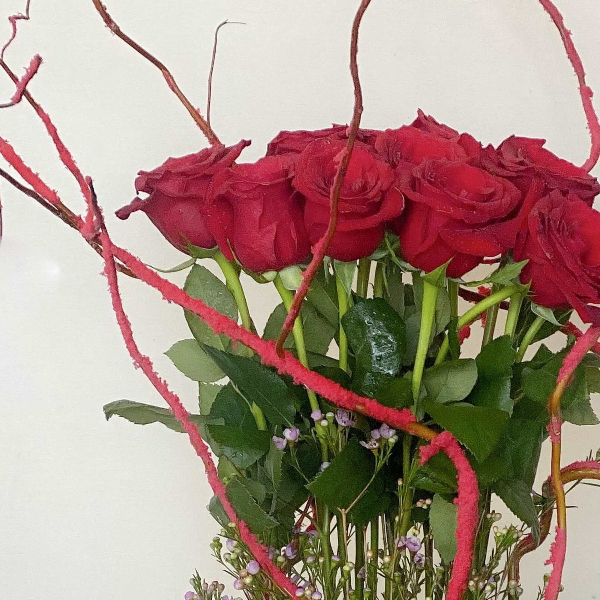 Red roses arranged with pink curly branches and small purple filler flowers