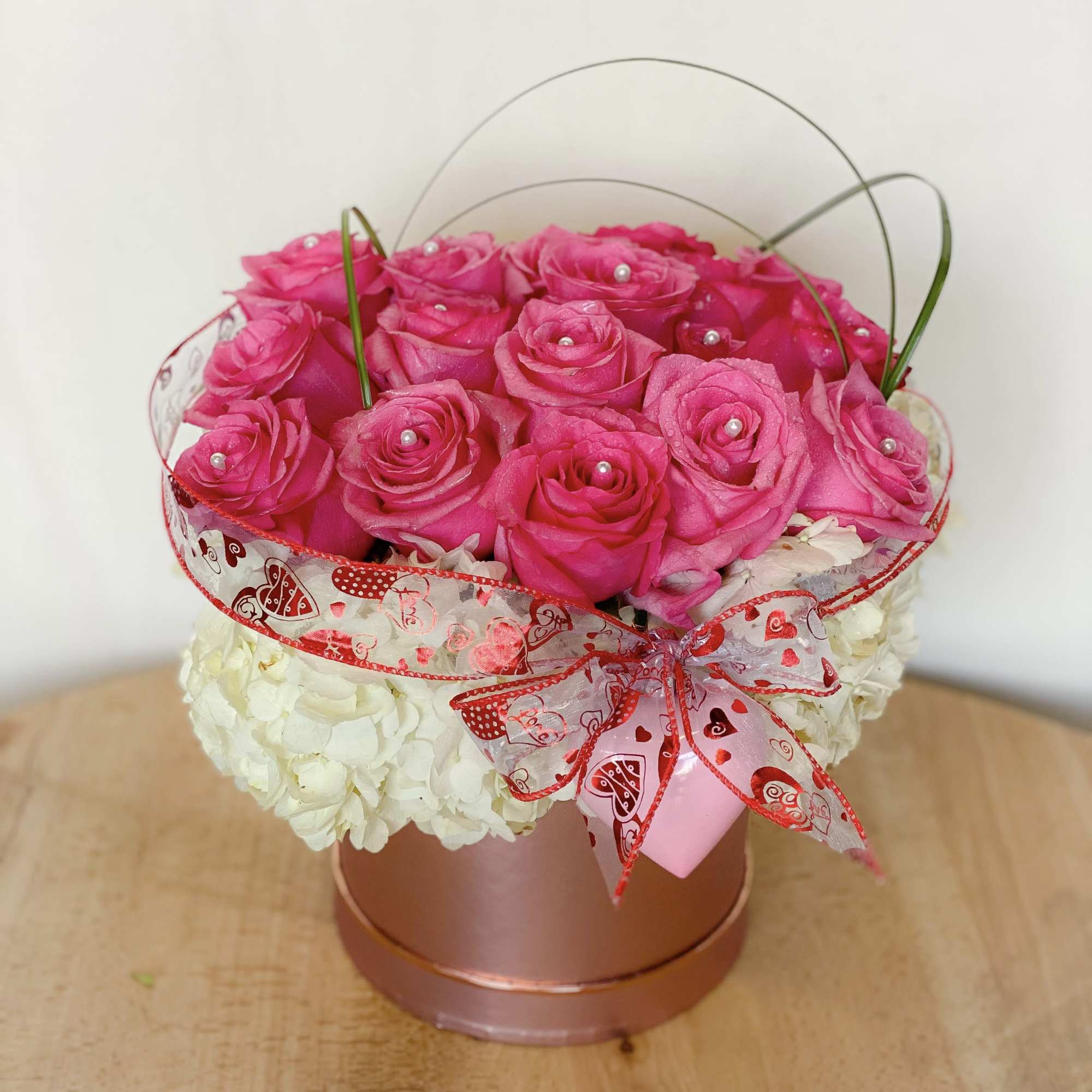 Pink roses in a round box with white hydrangeas and a heart ribbon