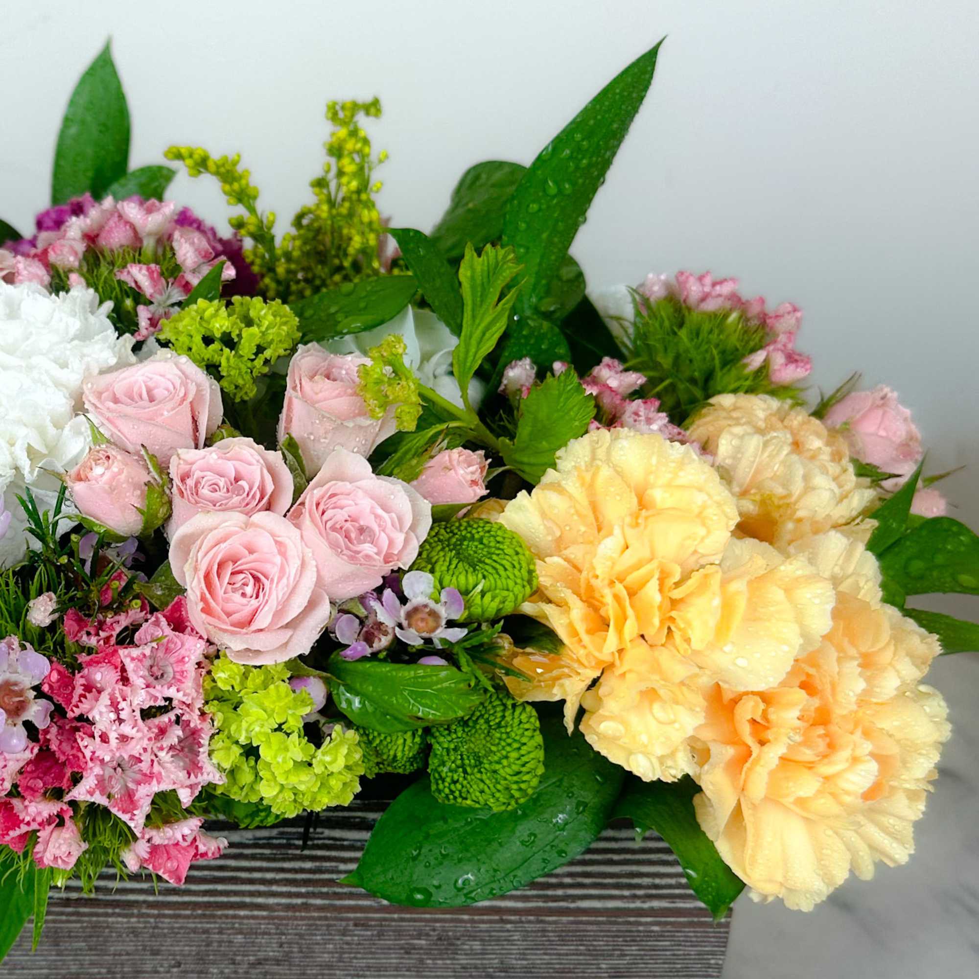 Mixed bouquet of pink roses, yellow carnations, and green pompons