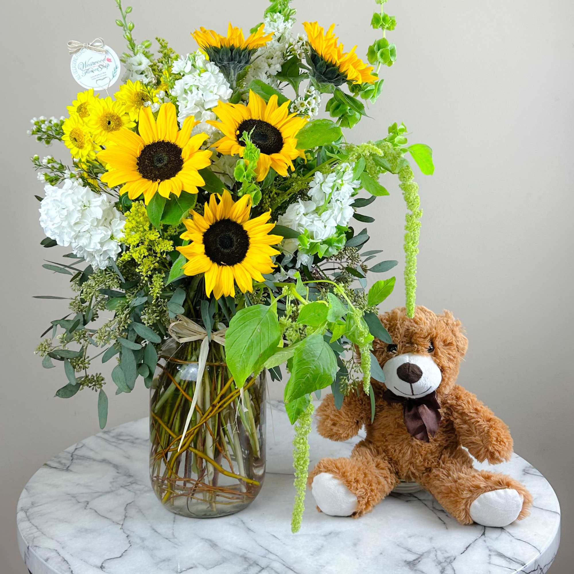 Sunflower bouquet in a glass vase beside a teddy bear