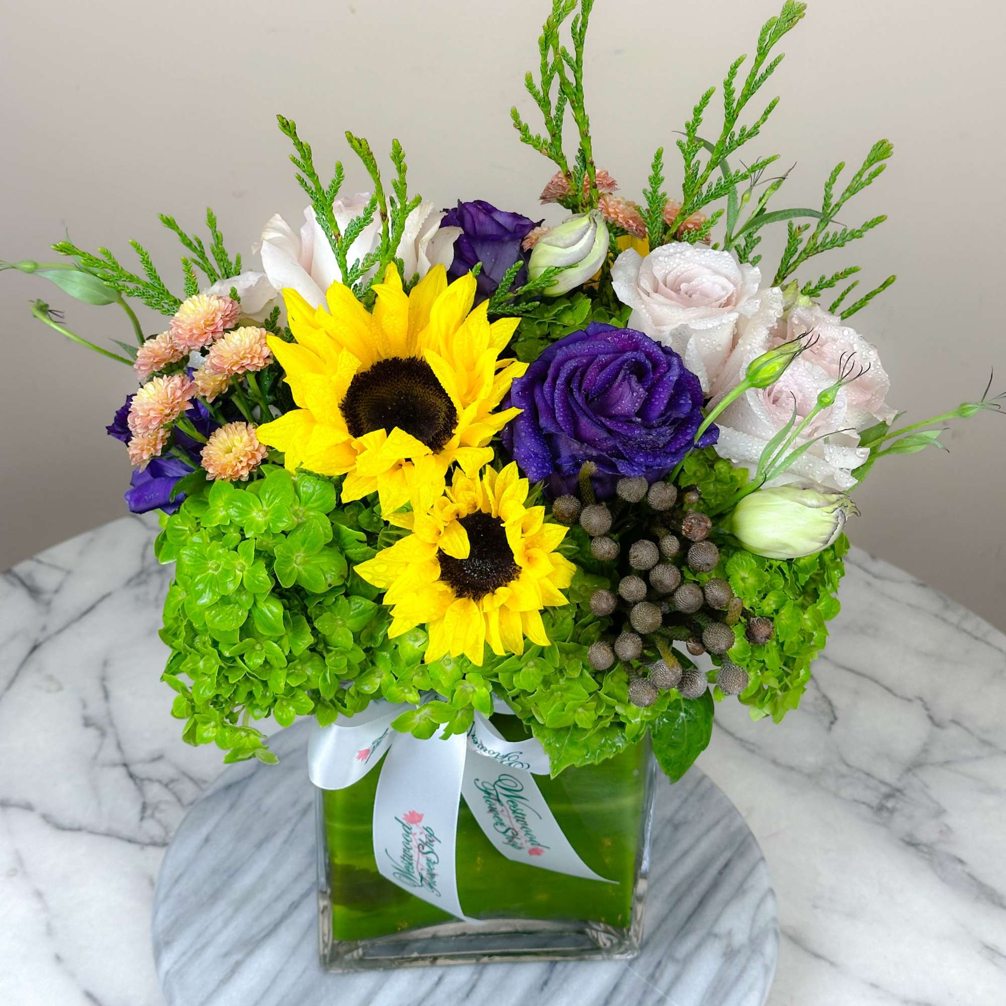 Bouquet of sunflowers, roses, and hydrangeas in a square glass vase
