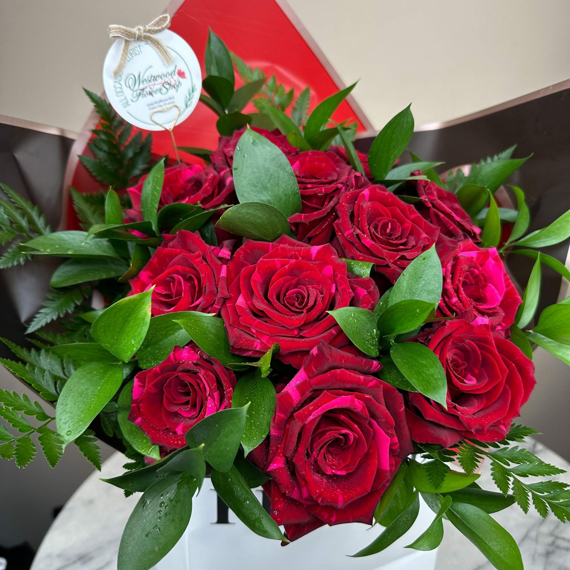 Bouquet of red roses with green foliage in a white box