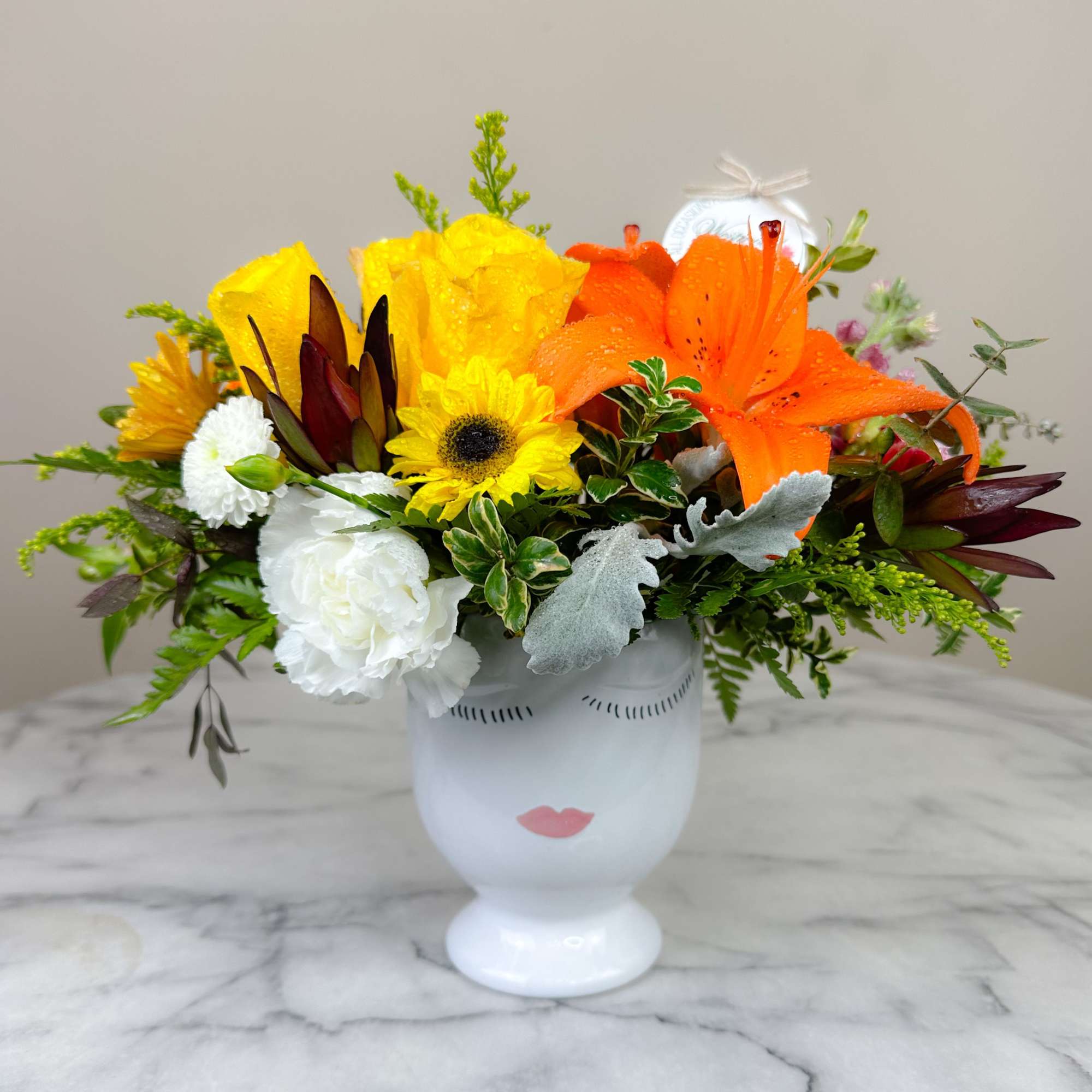 Bright mixed bouquet in a white face vase with orange lilies and yellow blooms