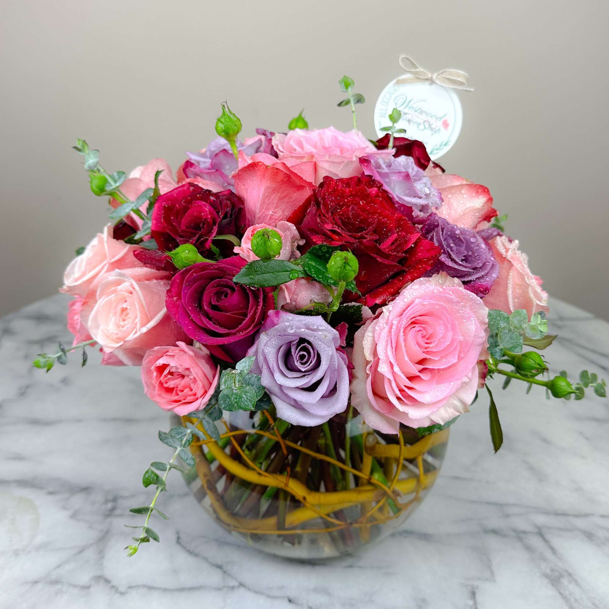 Mixed roses in pink, red, and lavender arranged in a glass vase