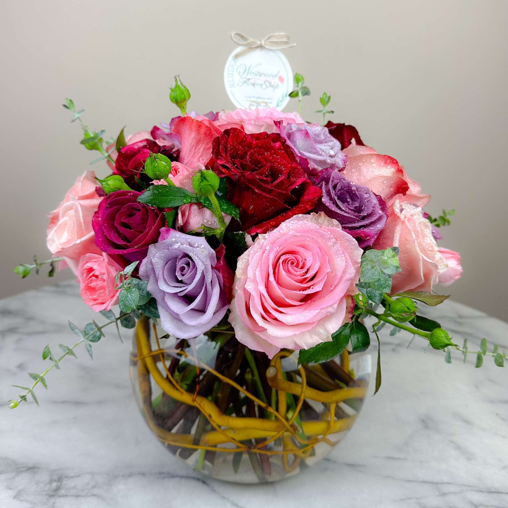 Mixed roses in pink, red, and lavender arranged in a glass vase.