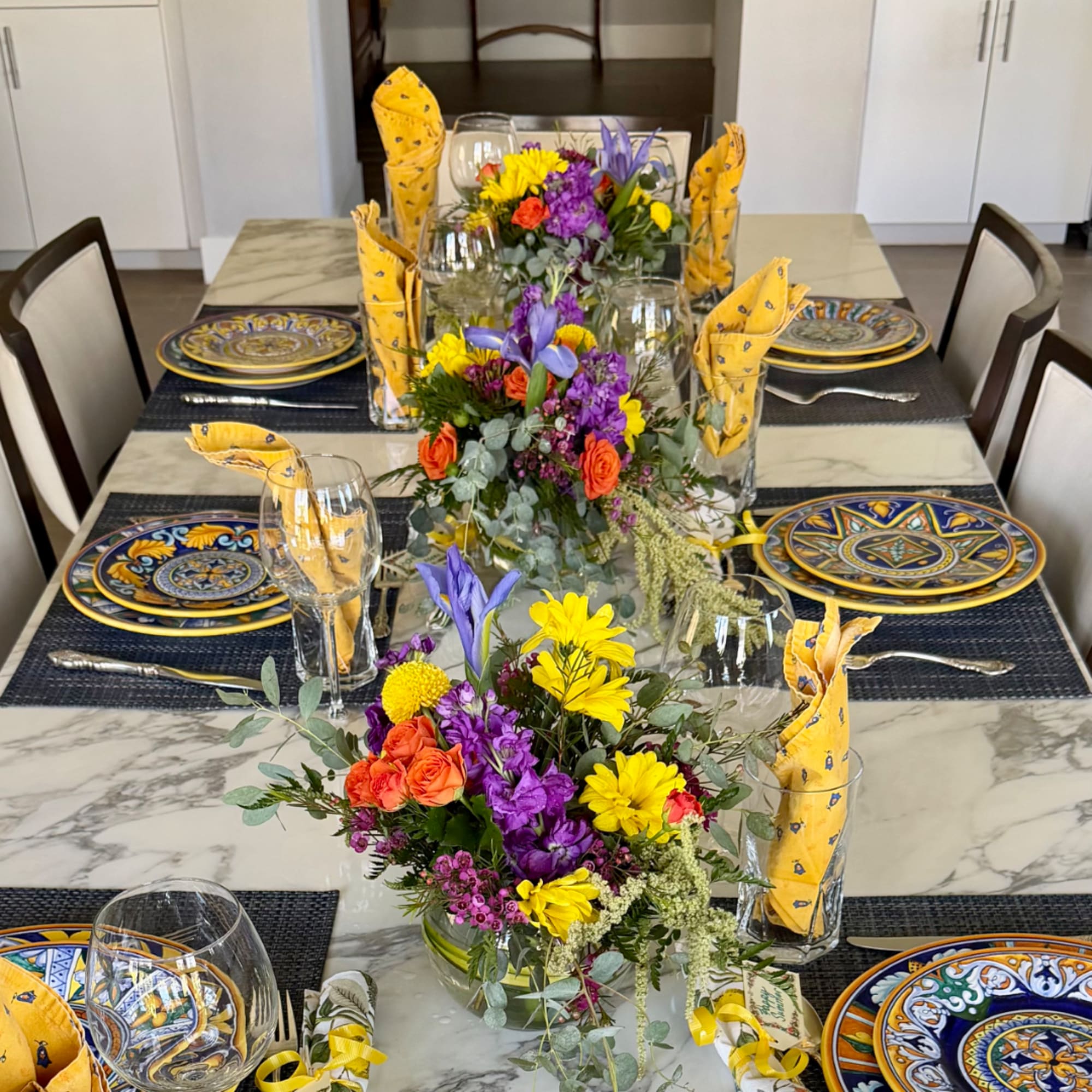 Colorful floral centerpieces on a set dining table with patterned plates and yellow napkins.