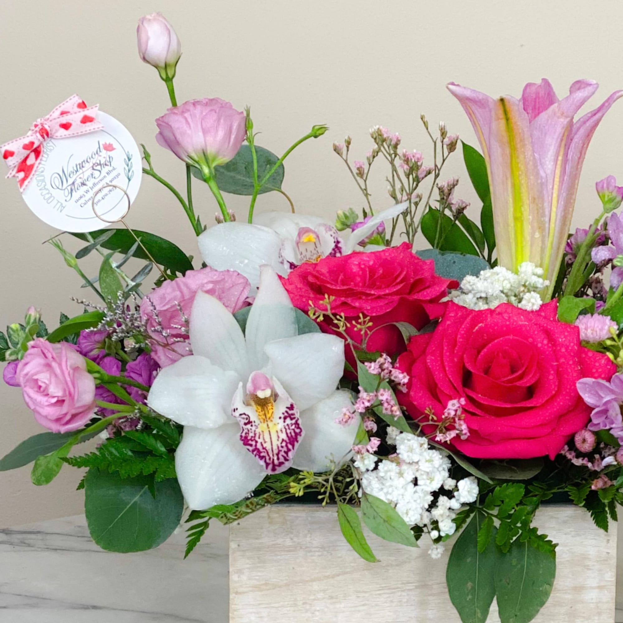 Pink and white floral arrangement in a wooden box with roses and orchids