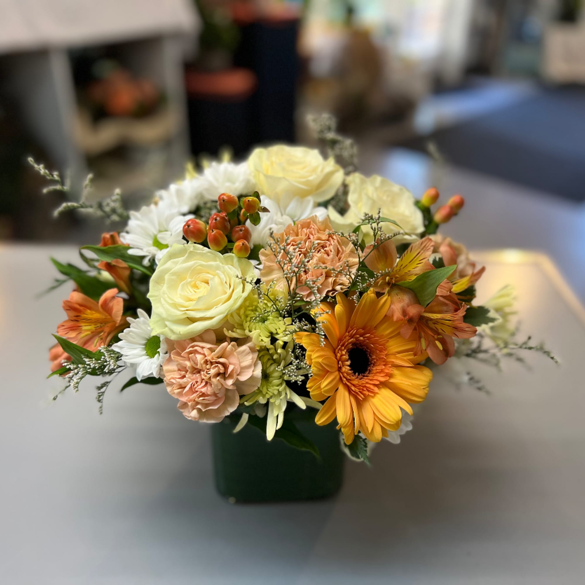 Mixed bouquet in a dark green vase with yellow, peach, and white flowers