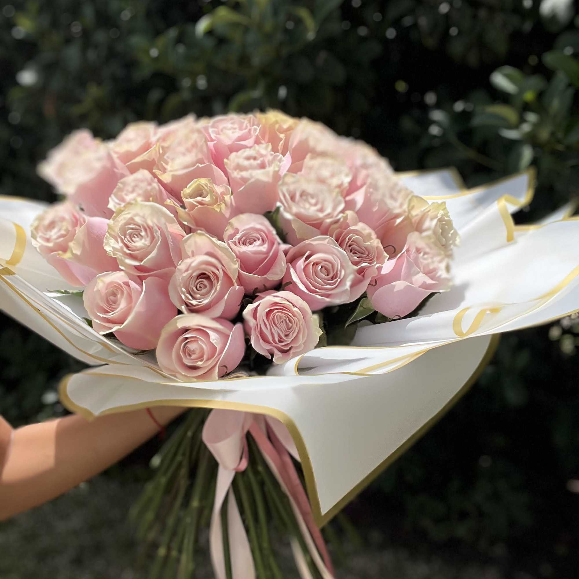 Bouquet of pale pink roses wrapped in white paper with gold trim