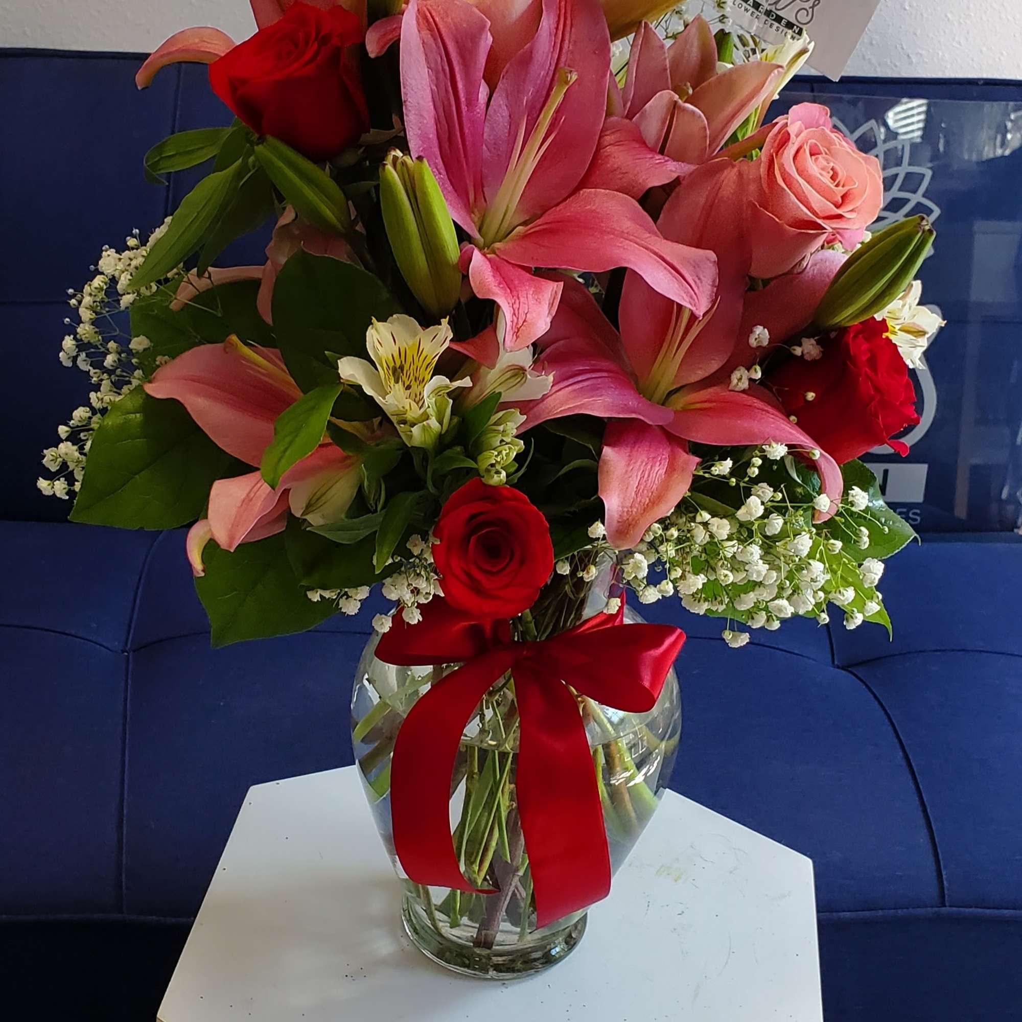 Pink lilies and roses arranged in a glass vase with a red ribbon