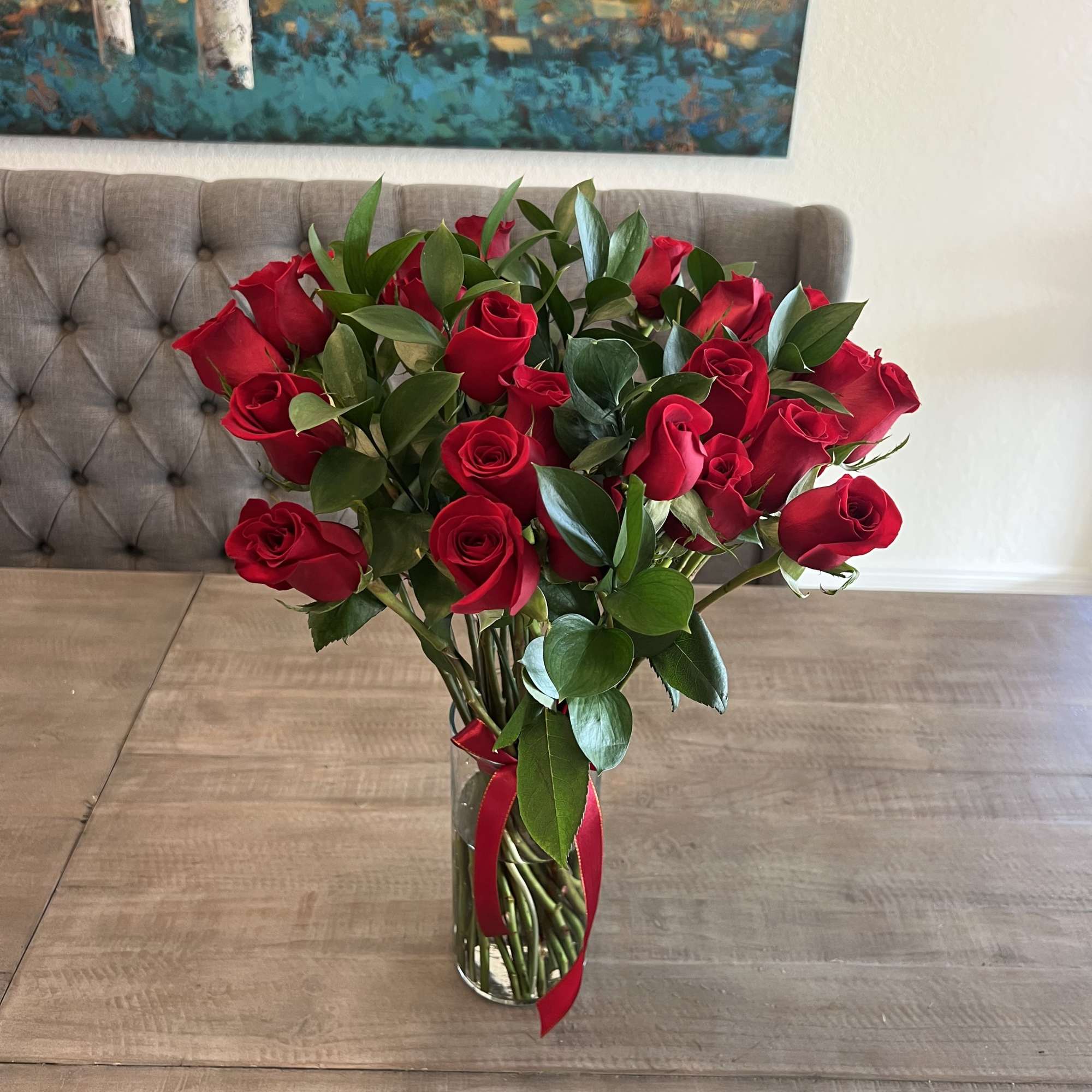 Red roses in a clear glass vase with a red ribbon