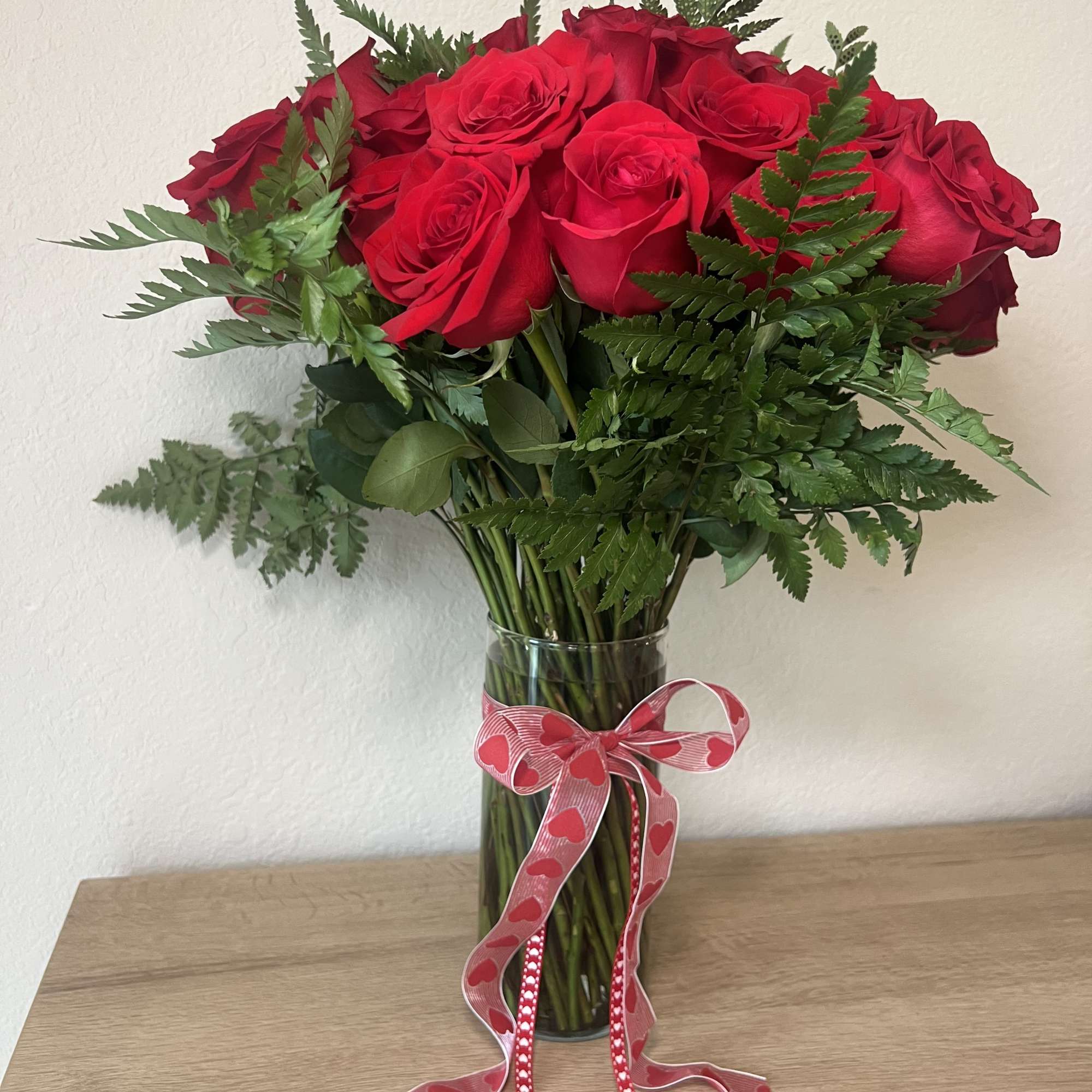 Red roses in a glass vase with a pink heart ribbon