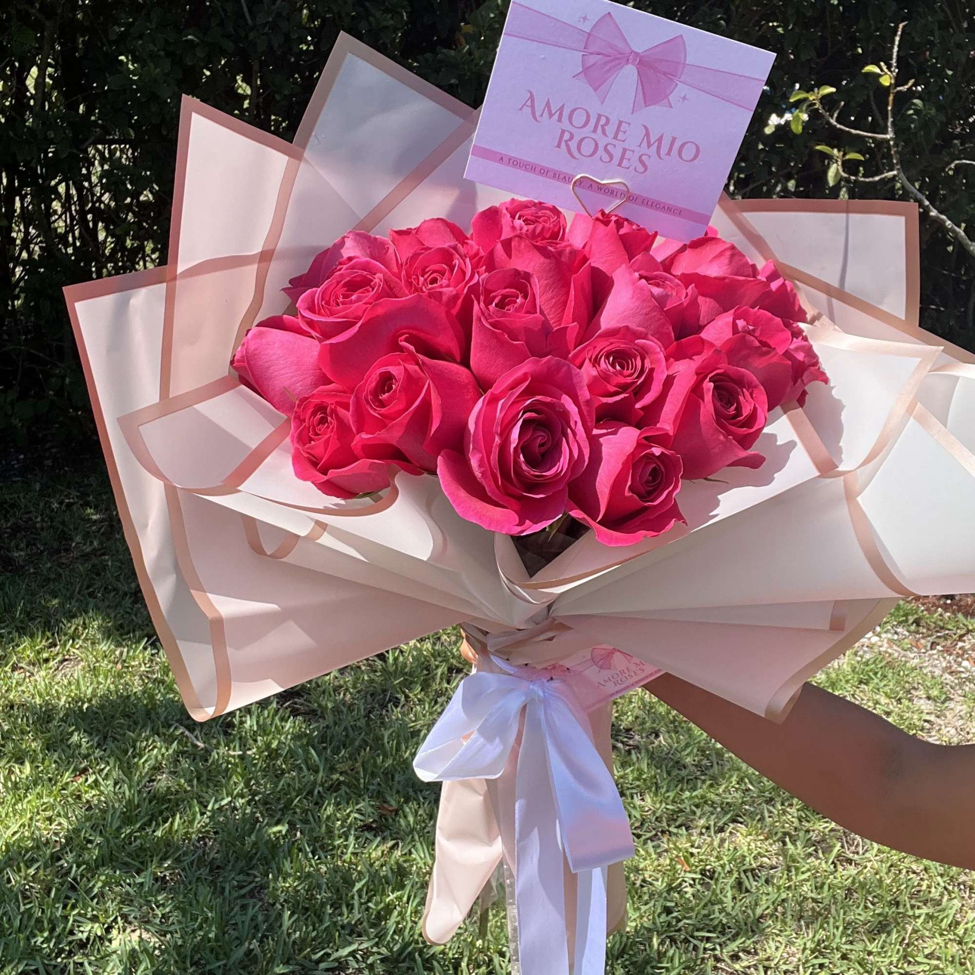 Bouquet of bright pink roses wrapped in blush paper with a white ribbon