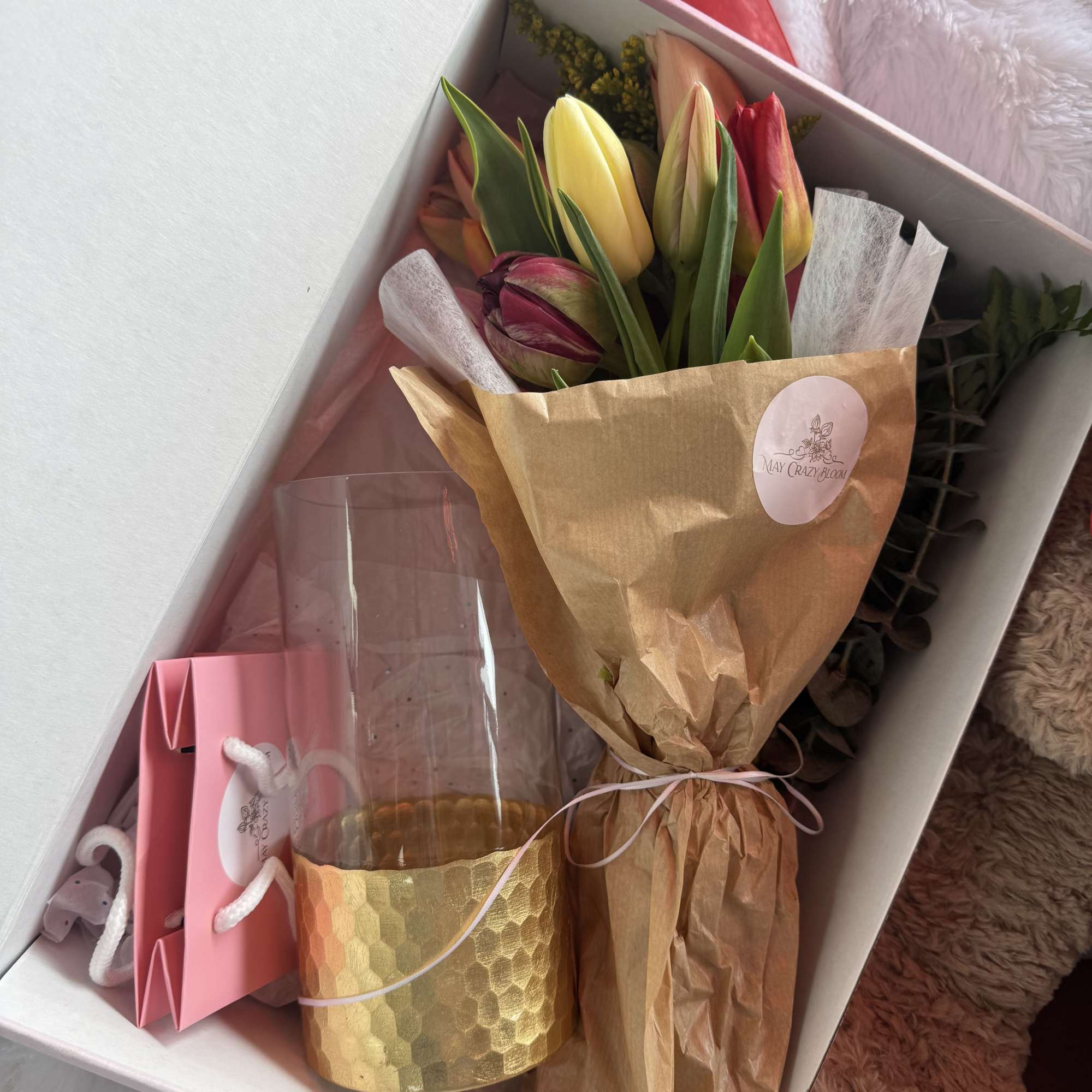 Boxed bouquet of multicolored tulips with a gold candle and pink gift bag