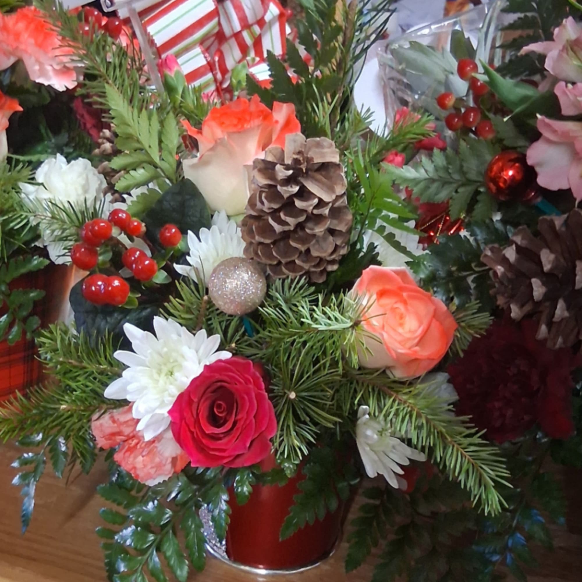 Holiday floral arrangement with roses, daisies, pinecones, and red berries in a red vase