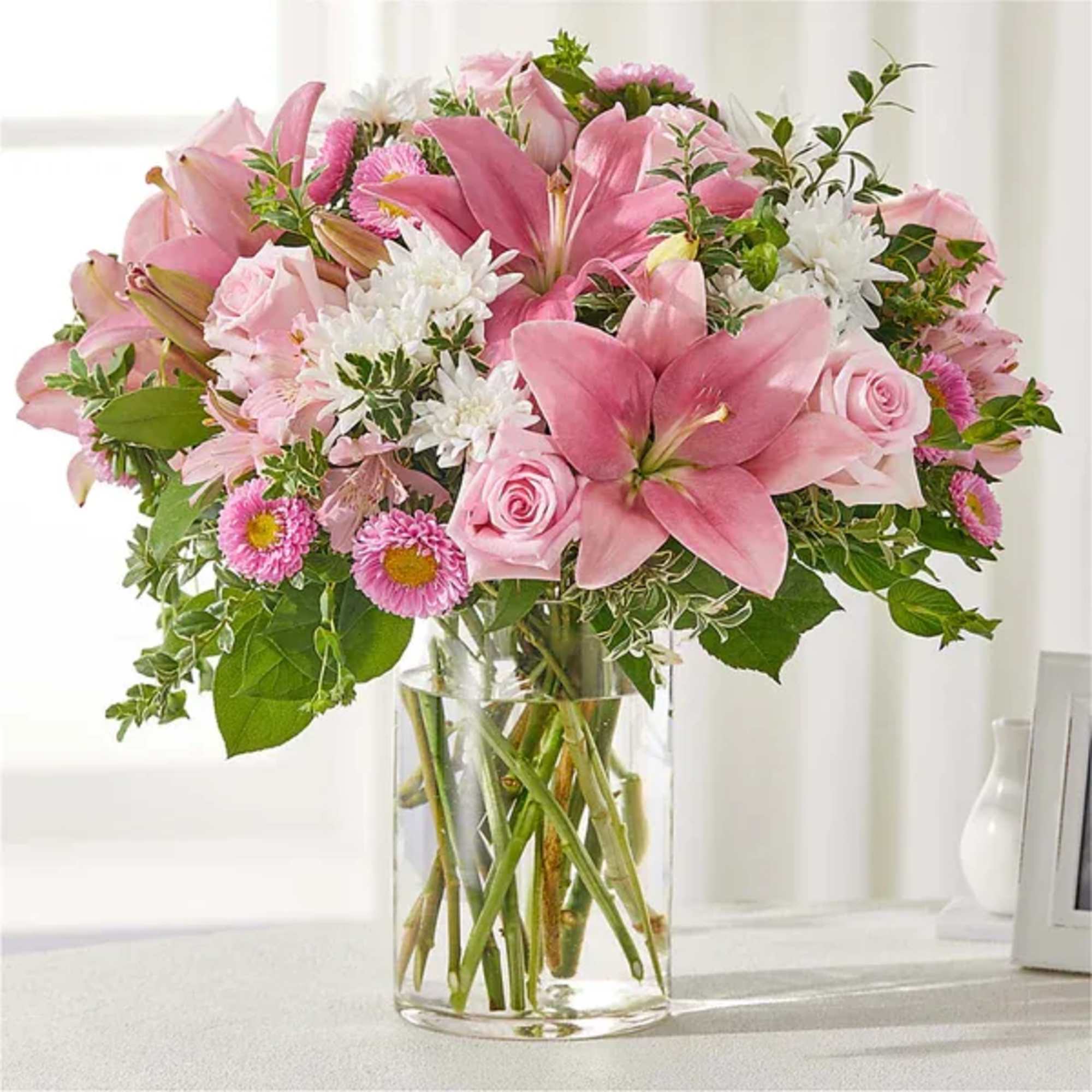 Pink lilies and roses arranged in a clear glass vase with white daisies