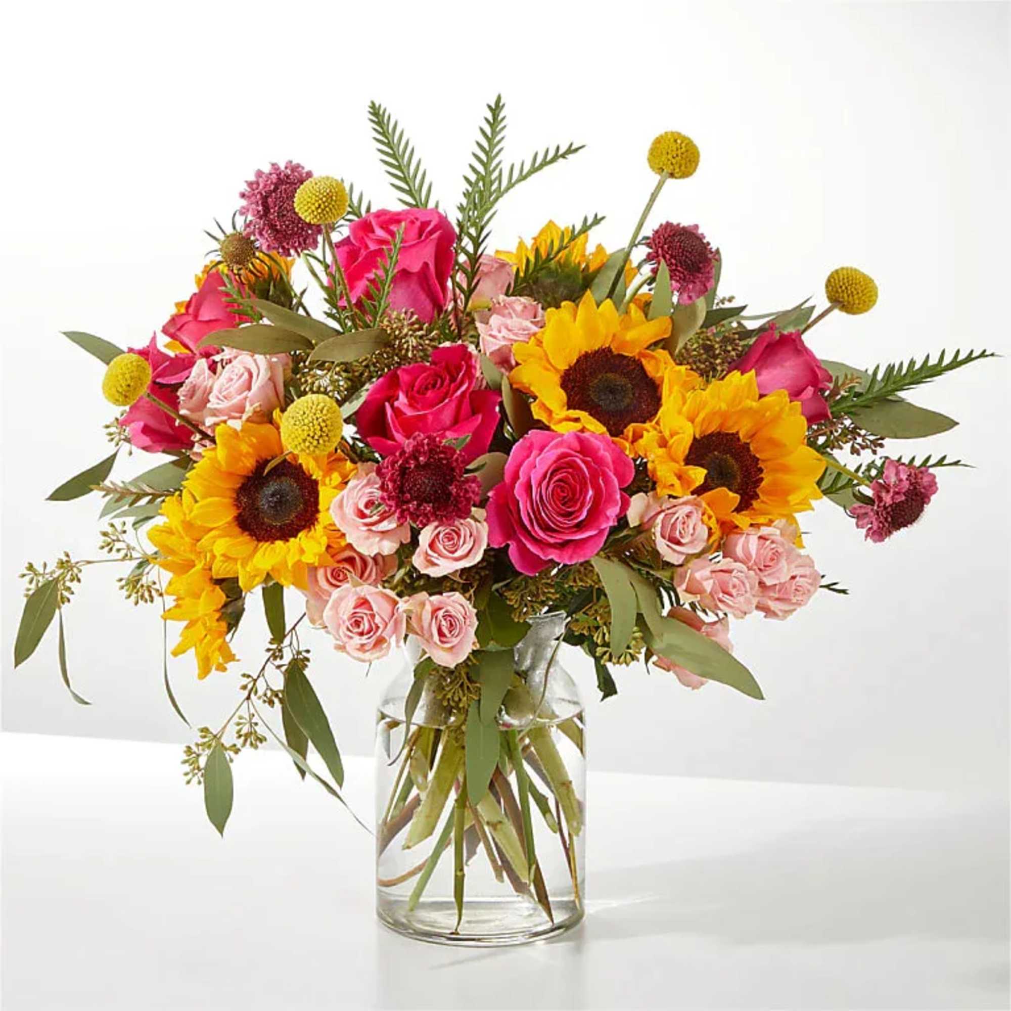 Bouquet of sunflowers, pink roses, and small yellow blooms in a glass vase