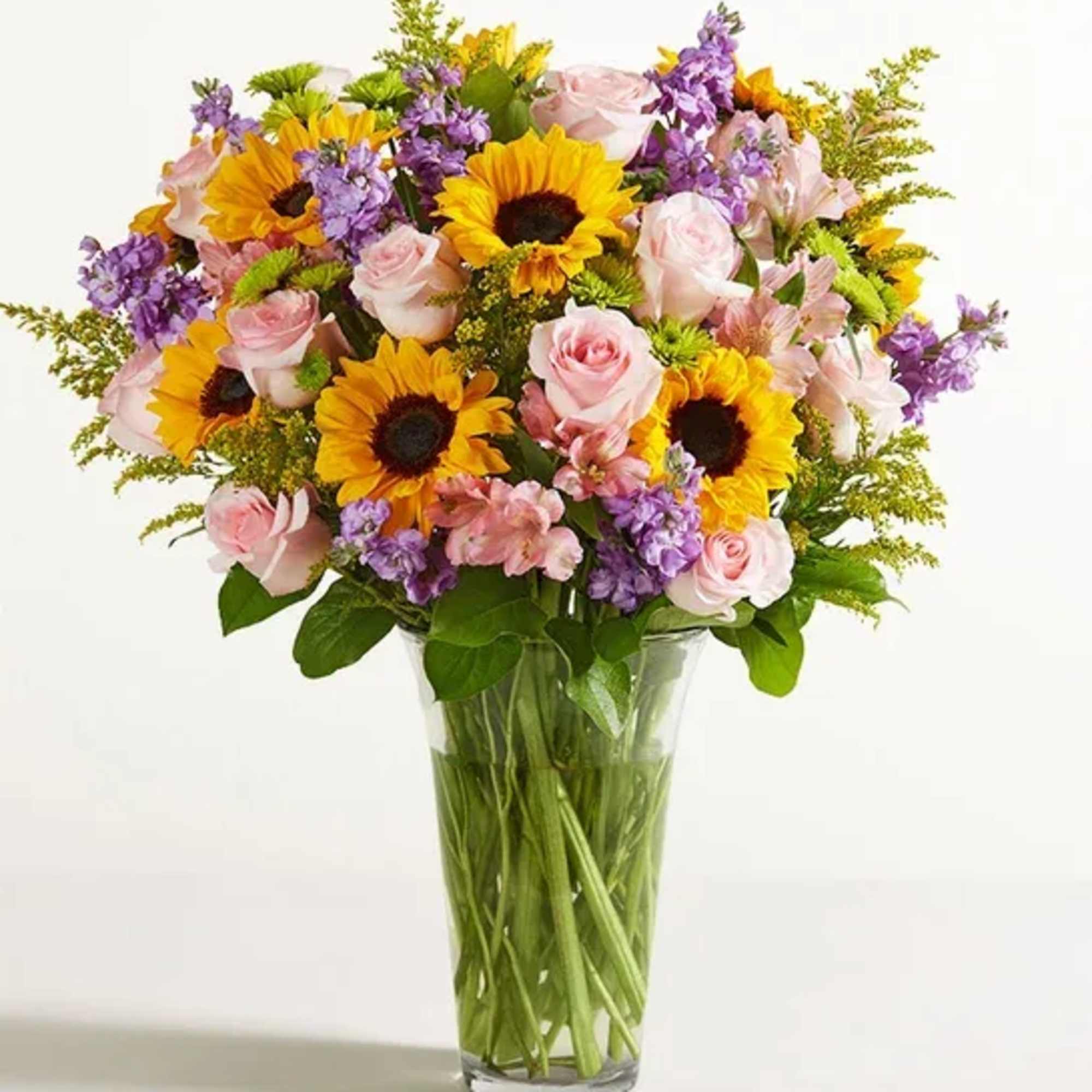 Bouquet of sunflowers, pink roses, and purple flowers in a clear glass vase