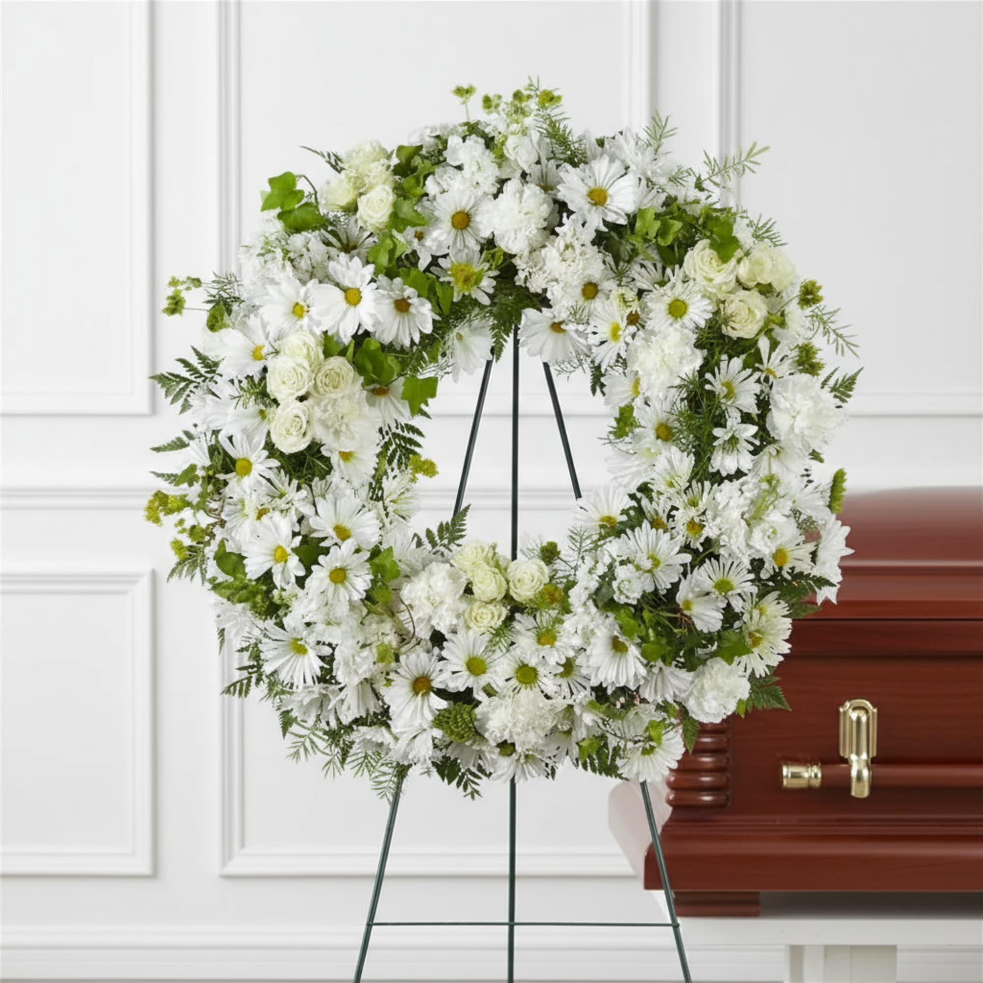 White floral wreath on an easel beside a casket