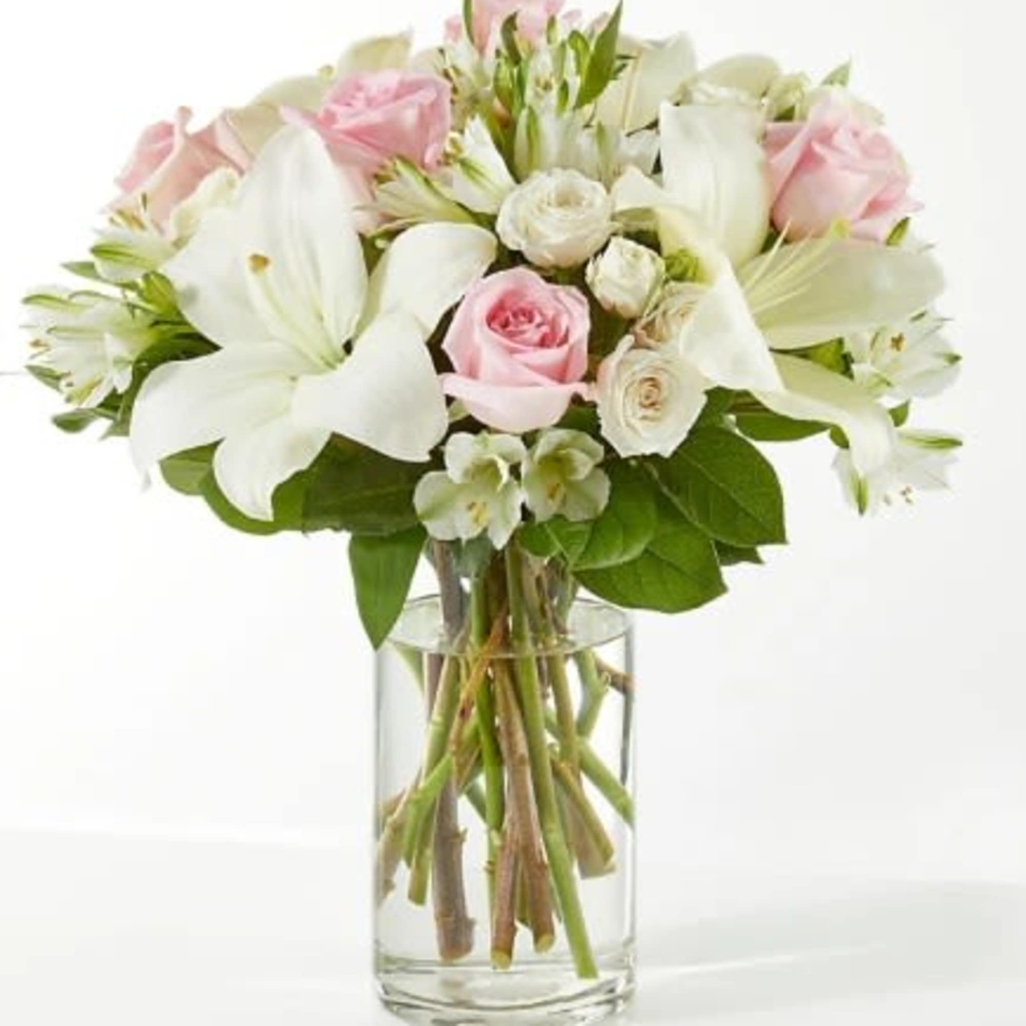 Pink roses and white lilies arranged with white blooms in a clear glass cylinder vase