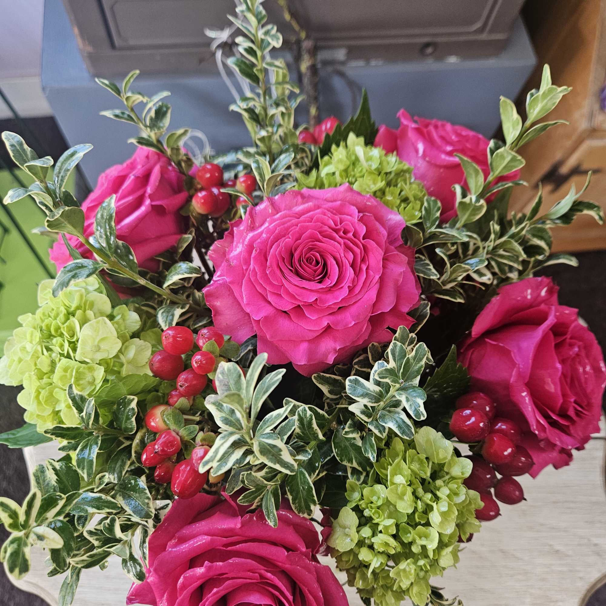 Arrangement of hot pink roses, green hydrangea clusters, and red berries in a compact design