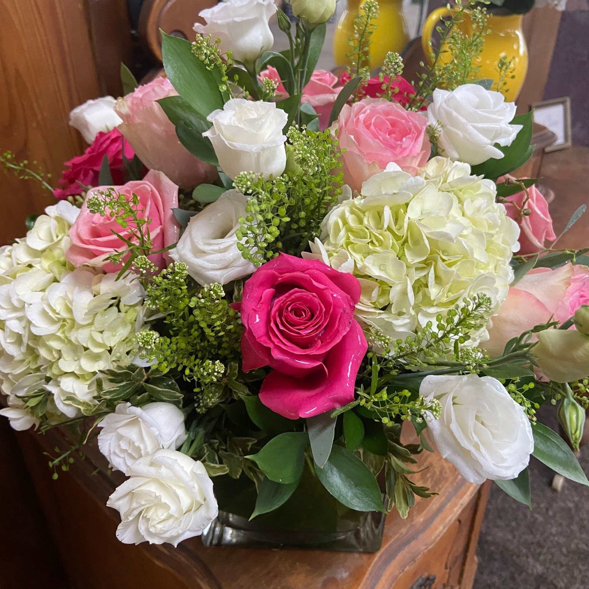Pink and white roses with white and green hydrangeas in a clear glass cube vase