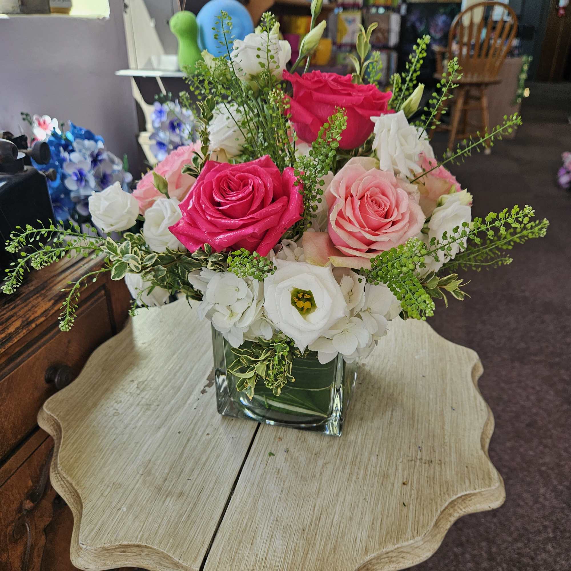 Pink and white rose and lisianthus arrangement in a clear glass cube vase on a small wooden table