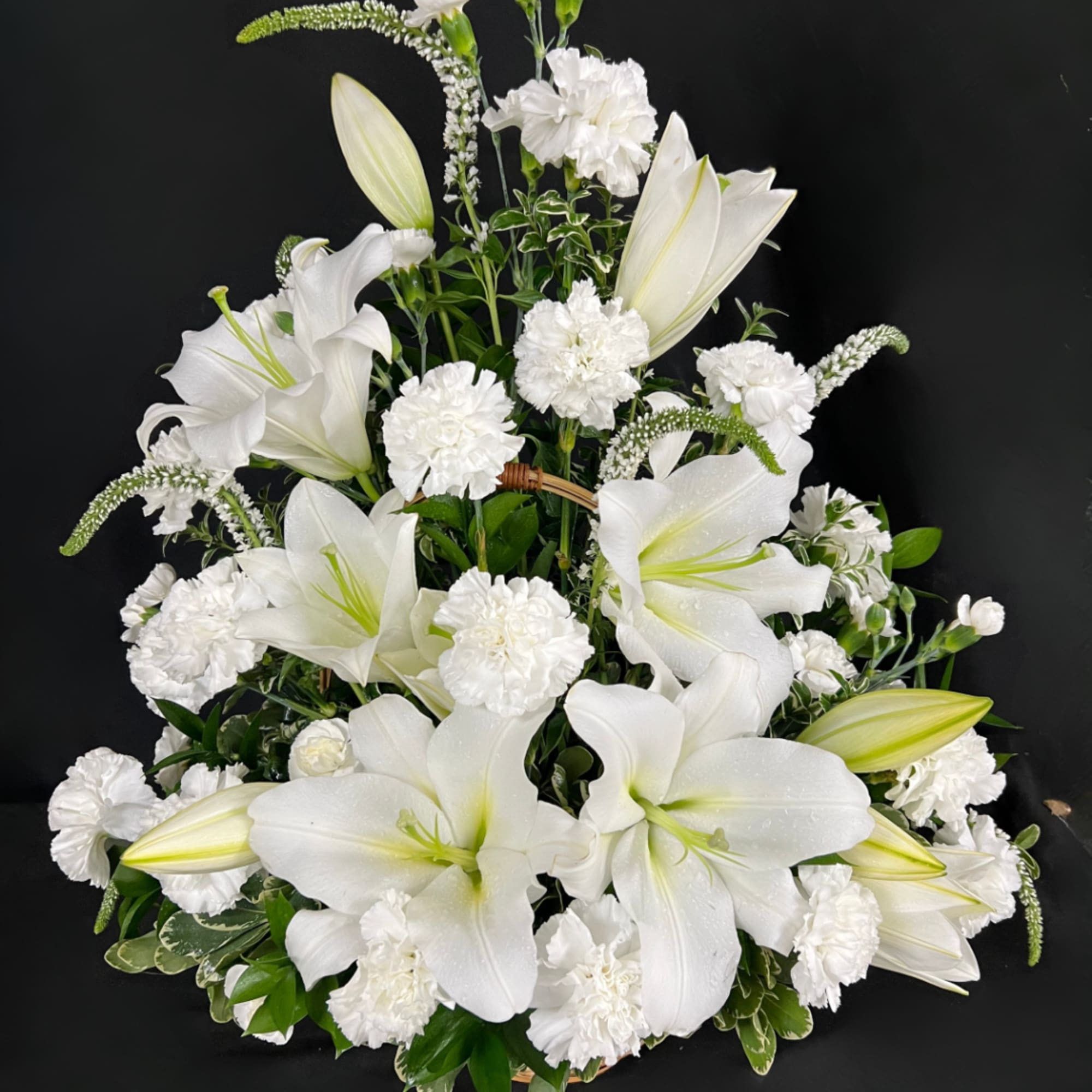 White lilies and carnations arranged in a basket on a black background