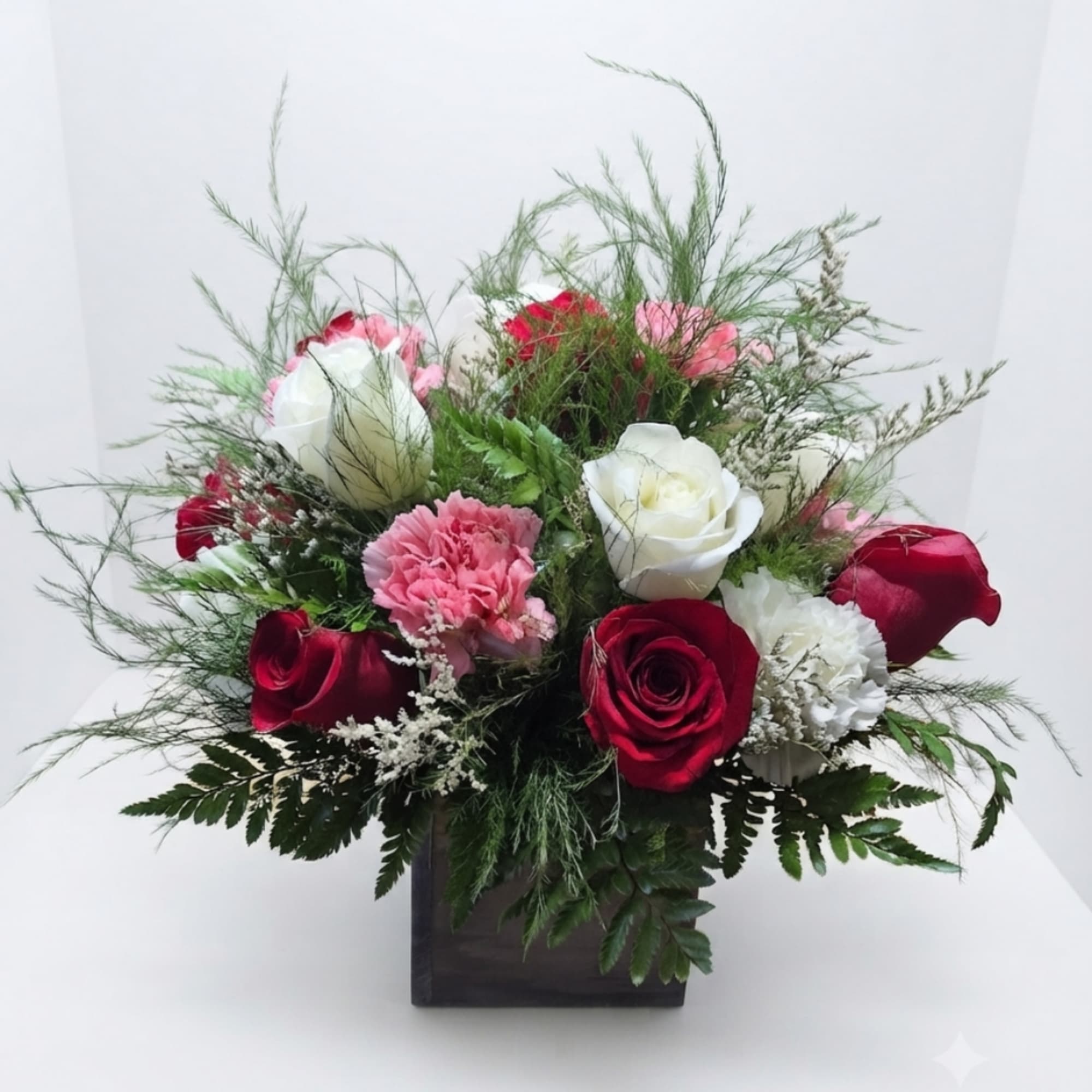 Red, white, and pink roses with carnations in a dark square vase