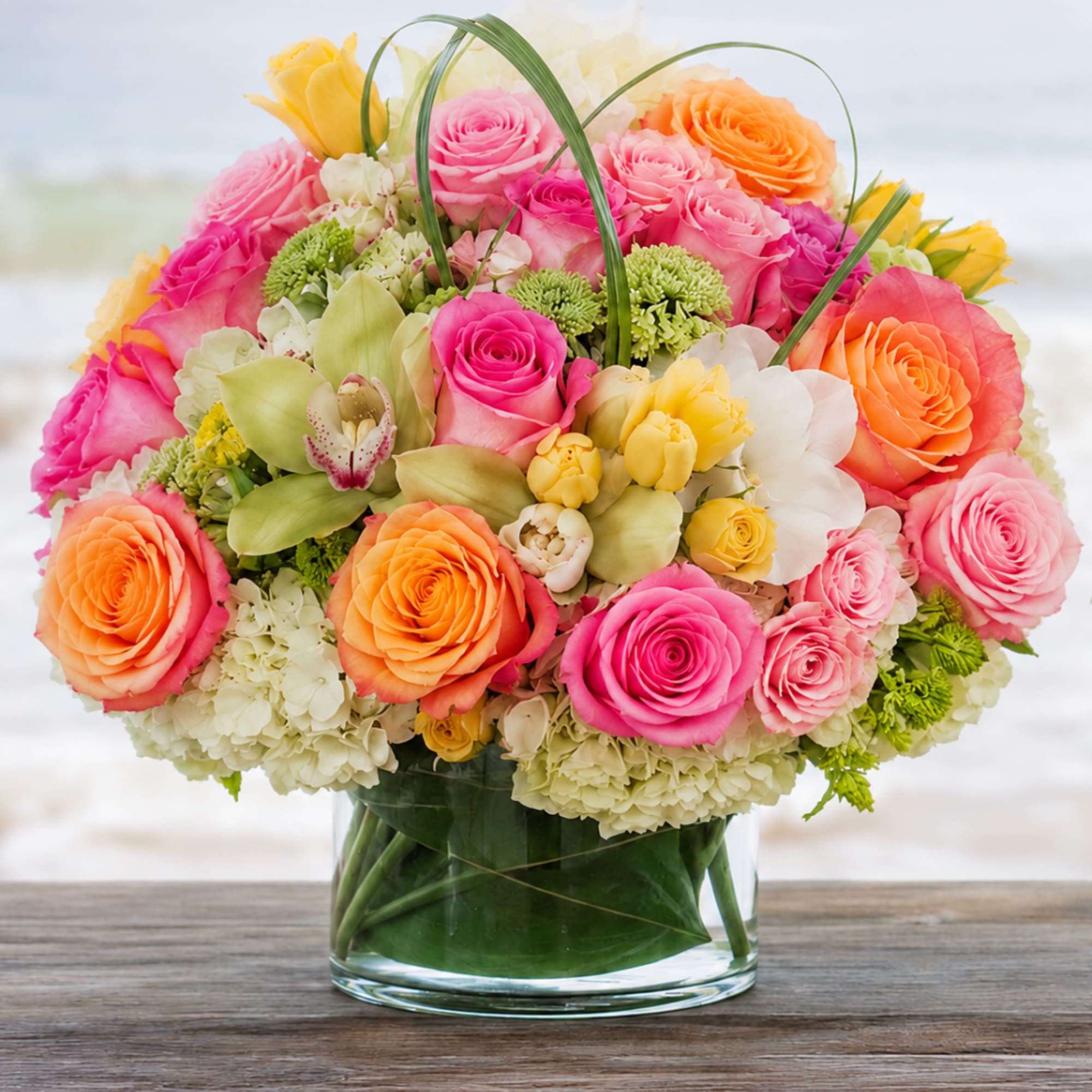 Mixed bouquet of pink, orange, and yellow roses in a glass vase