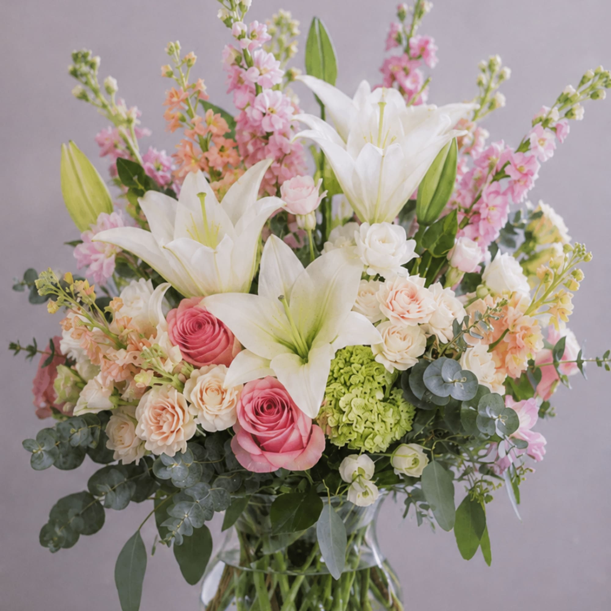 Bouquet of white lilies, pink roses, and pastel flowers in a glass vase