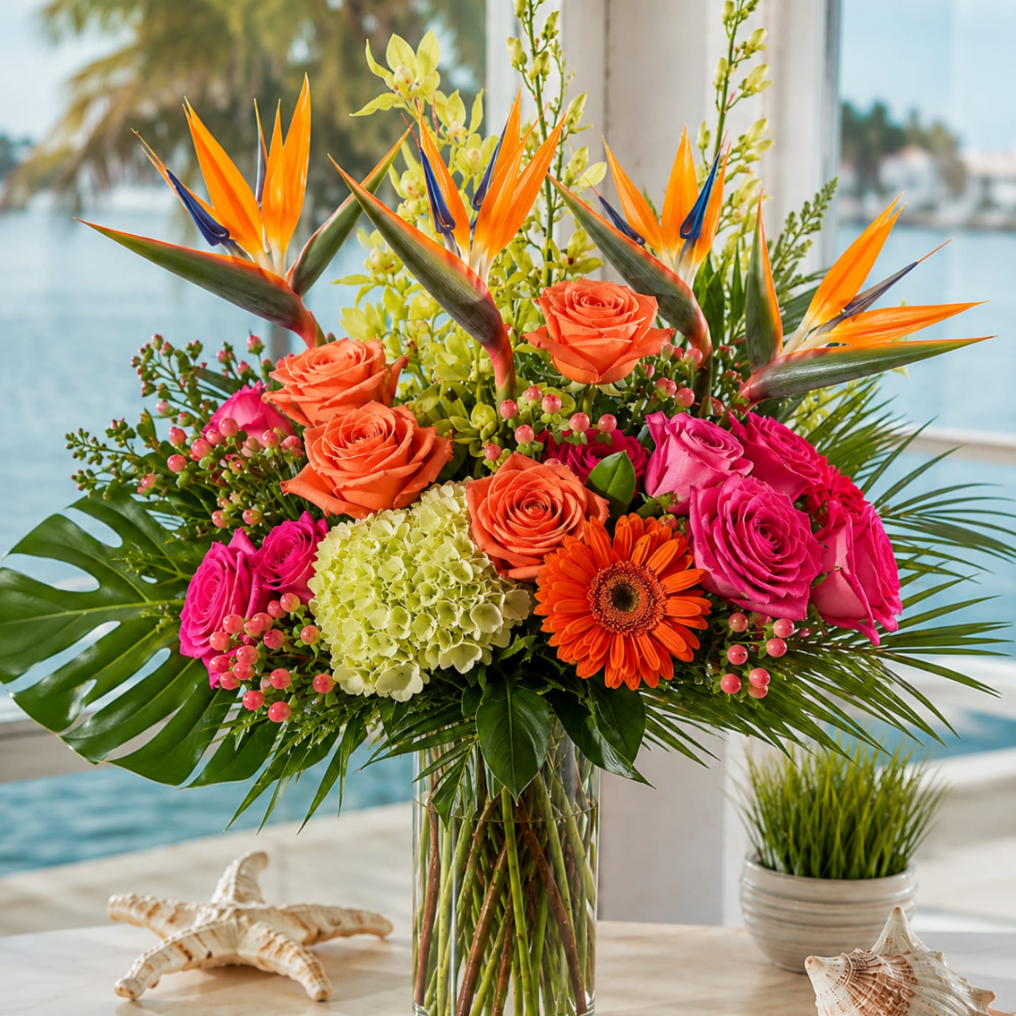 Tropical bouquet with orange roses, pink roses, and bird-of-paradise in a glass vase