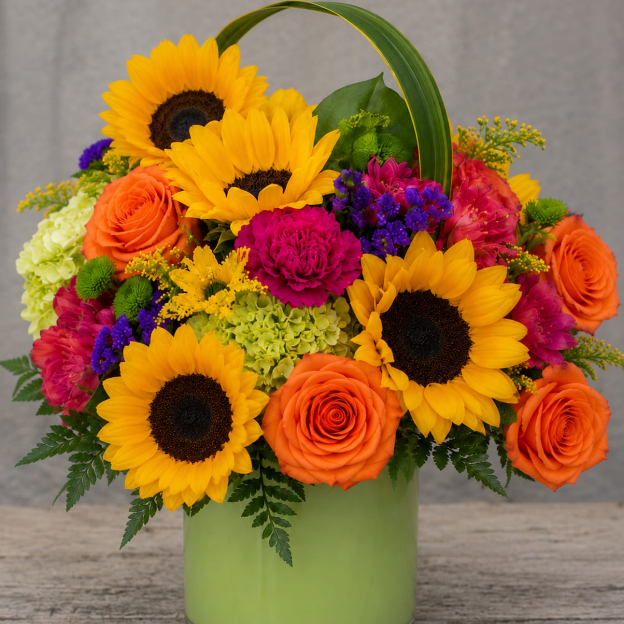 Bright mixed bouquet with sunflowers, orange roses, and pink blooms in a green vase