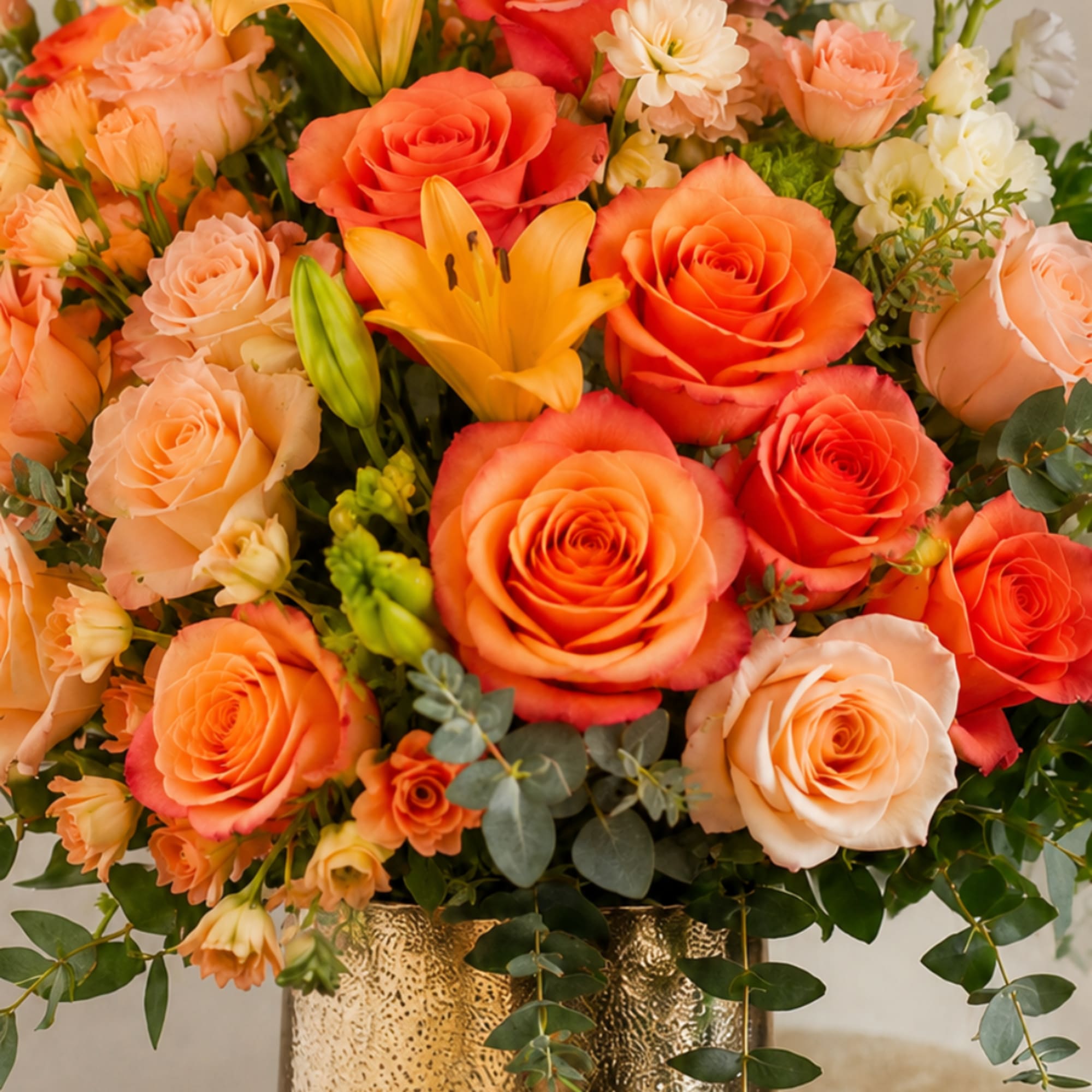 Orange and peach roses with a yellow lily in a gold vase