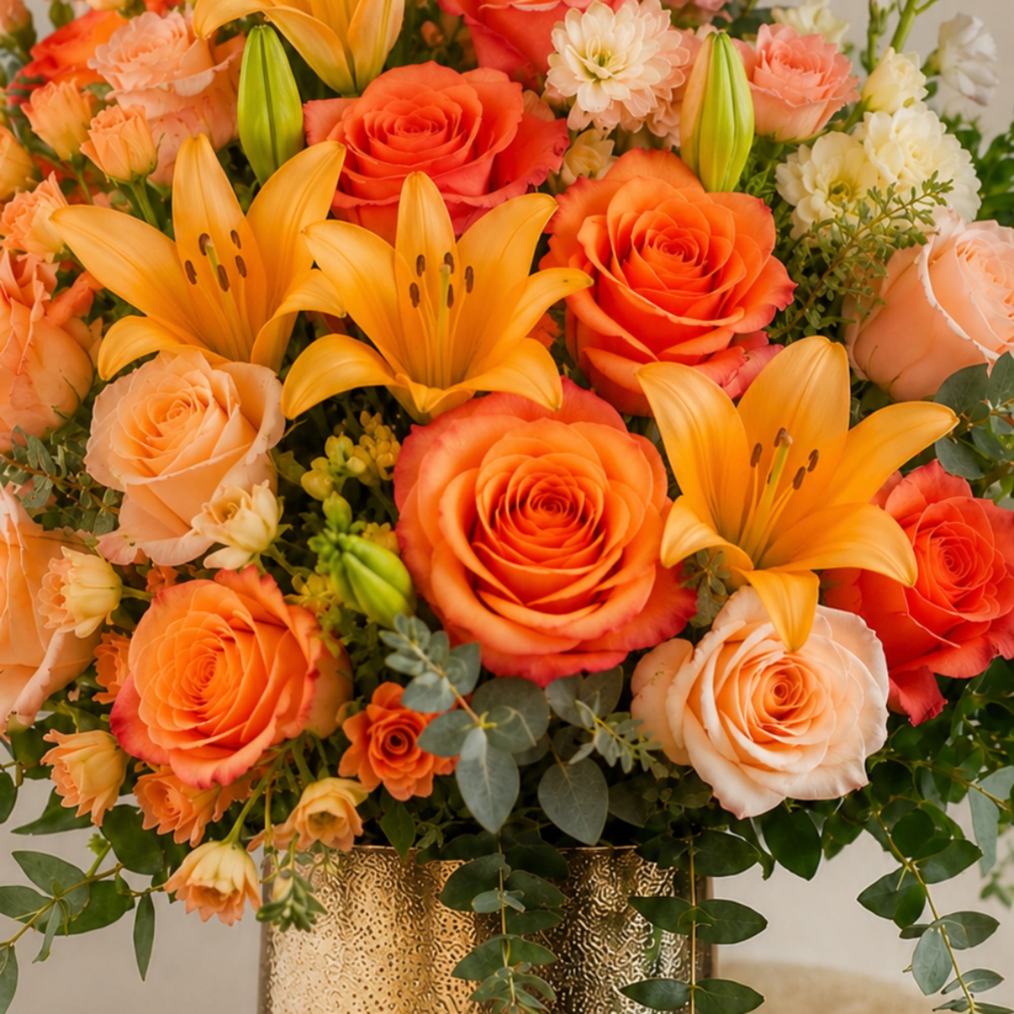Orange roses and yellow lilies arranged in a gold vase