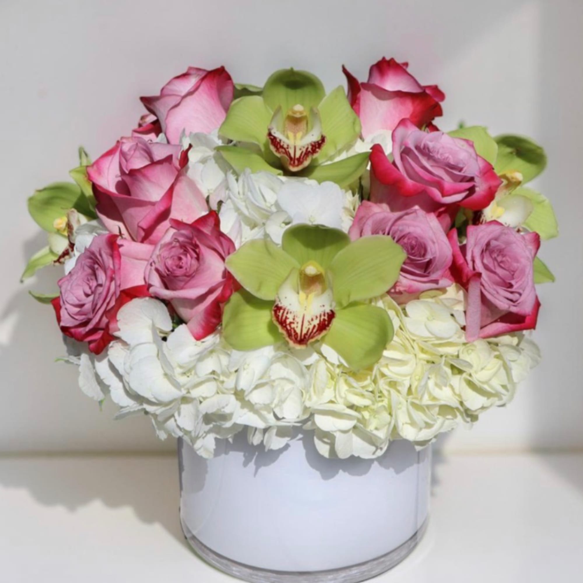 Pink roses and green orchids arranged with white hydrangeas in a white vase