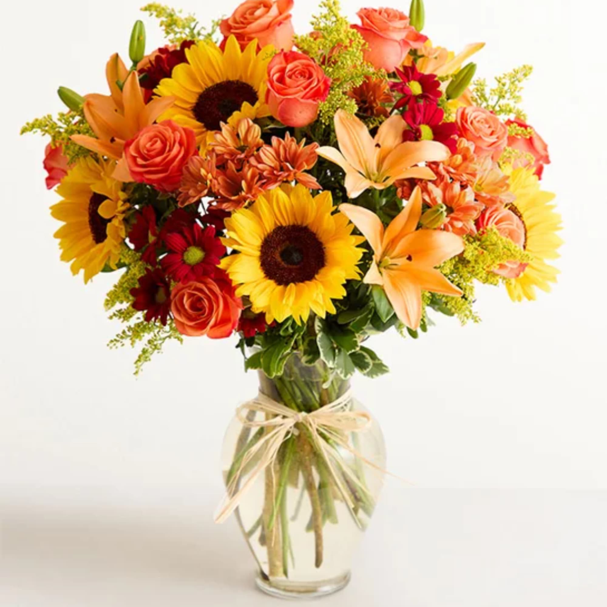 Mixed bouquet of sunflowers, roses, lilies, and orange flowers in a glass vase