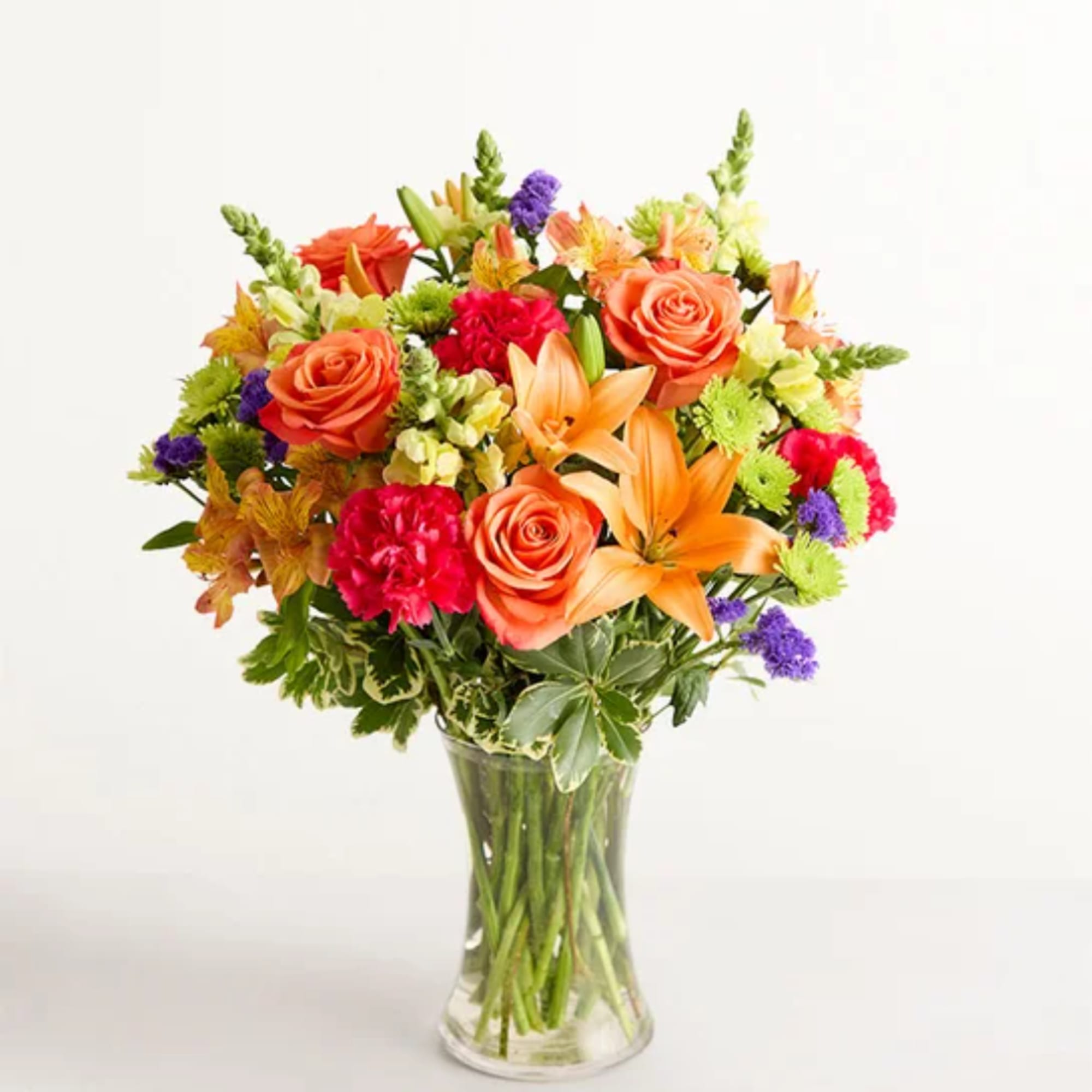 Mixed bouquet of orange roses, lilies, and bright accent flowers in a clear glass vase