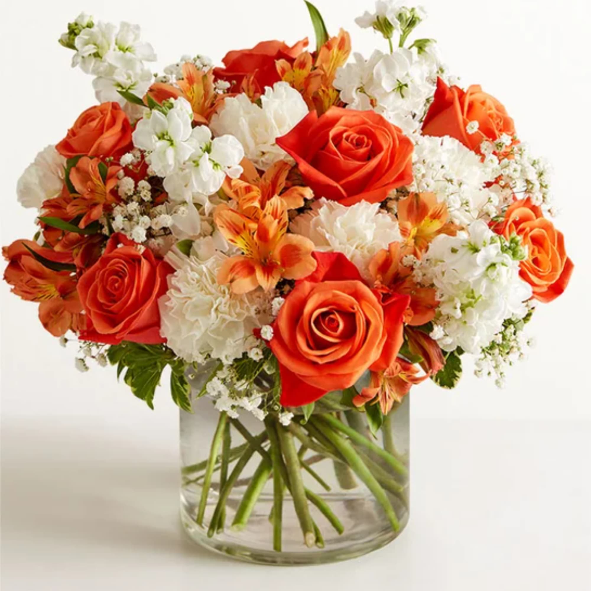 Orange roses and white flowers arranged in a clear glass vase