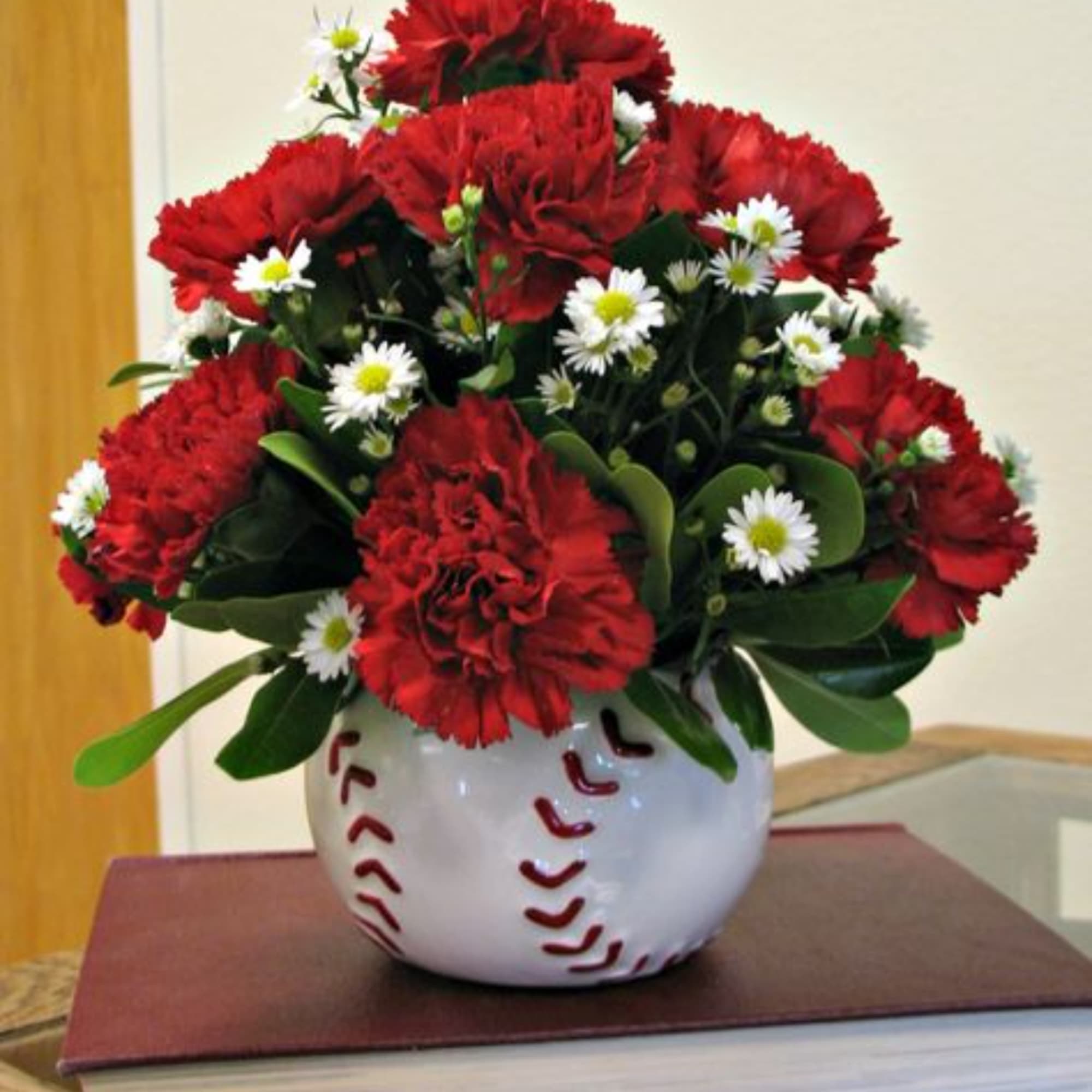 Red carnations and white daisies in a baseball-themed vase