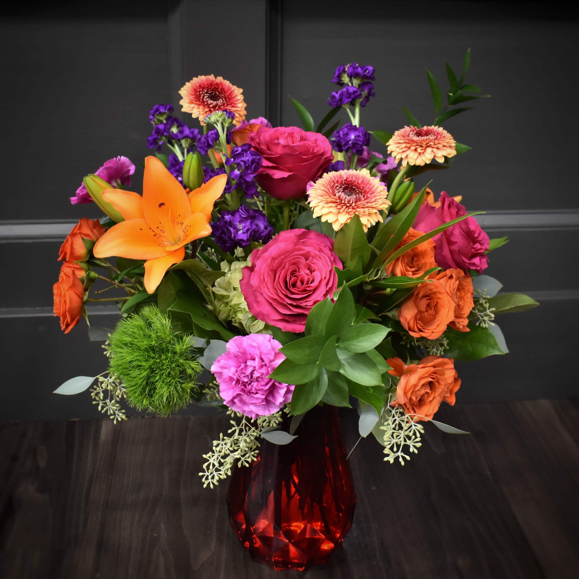Colorful bouquet of roses, lilies, and gerbera daisies in a red vase