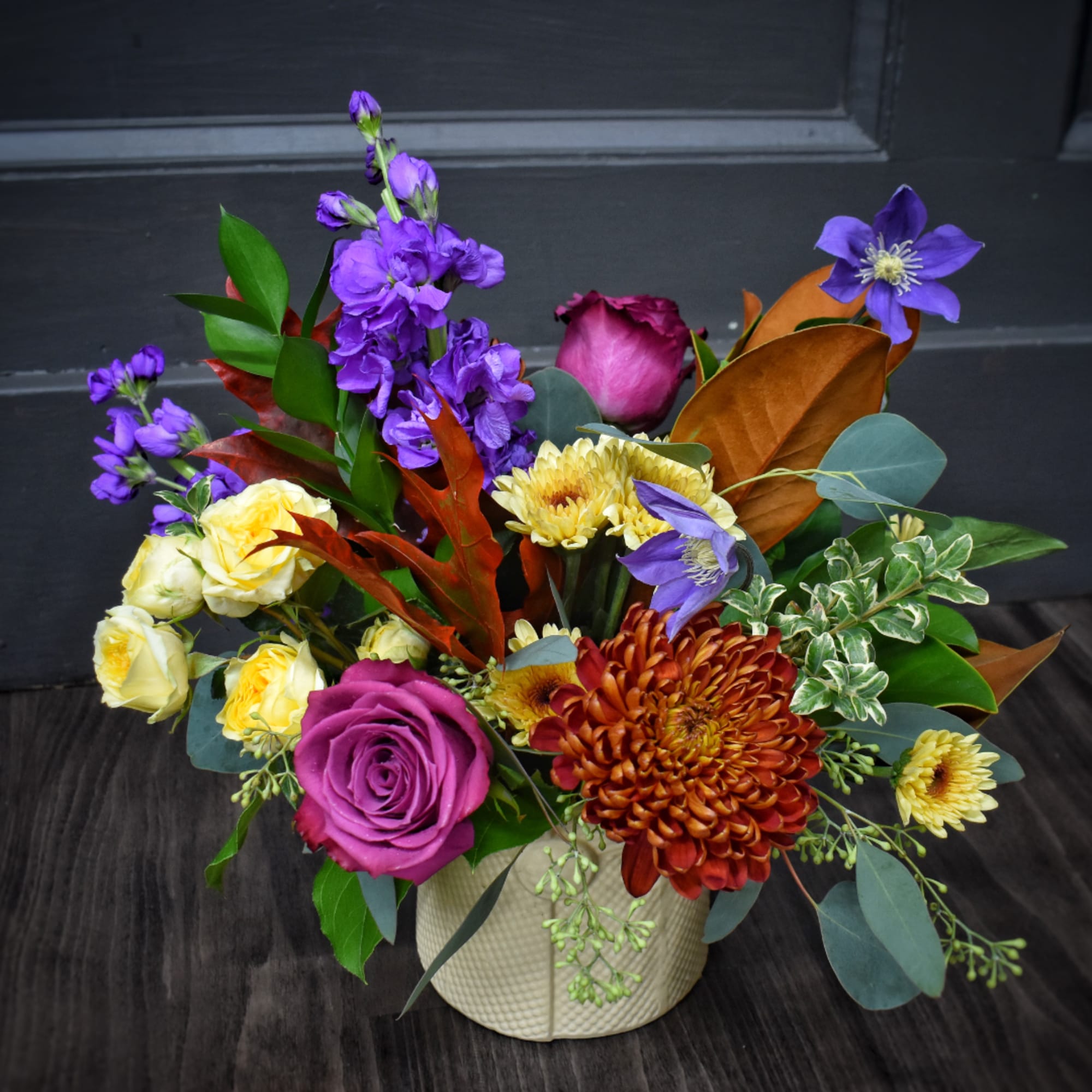 Colorful bouquet in a textured cream vase with purple, yellow, and orange flowers