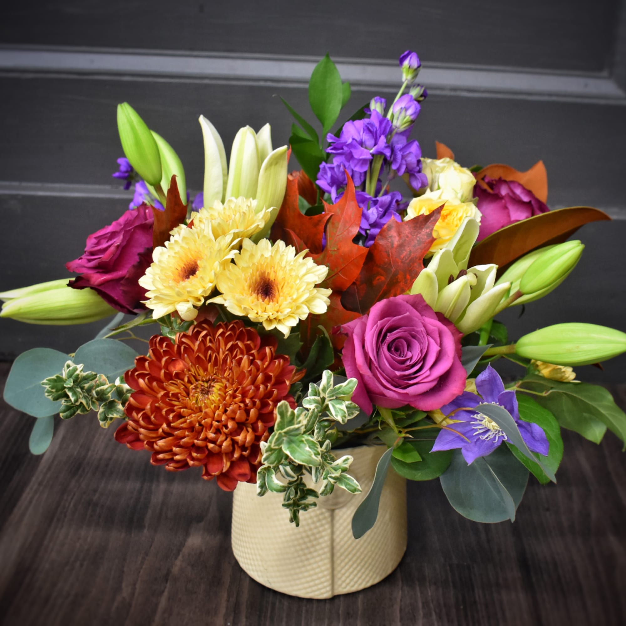Mixed bouquet of lilies, roses, and chrysanthemums in a cream vase