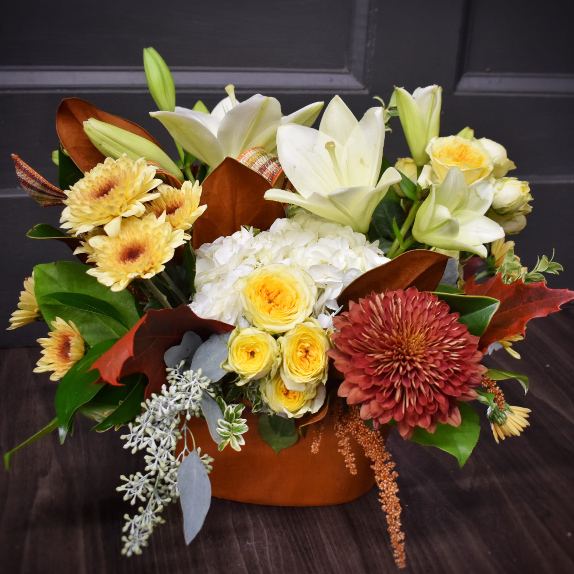 Mixed bouquet with white lilies, yellow roses, and chrysanthemums in a brown container