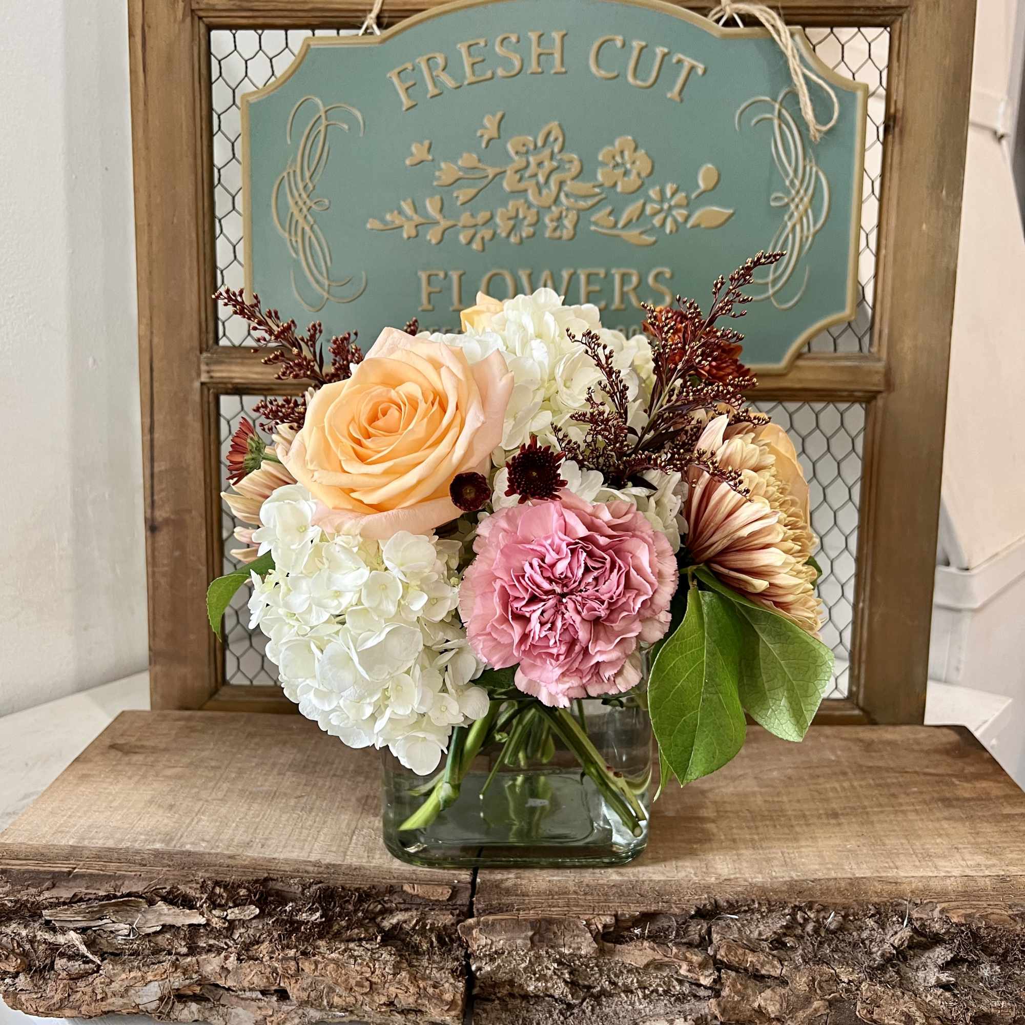 Mixed bouquet of peach roses, pink carnations, and white hydrangeas in a glass vase